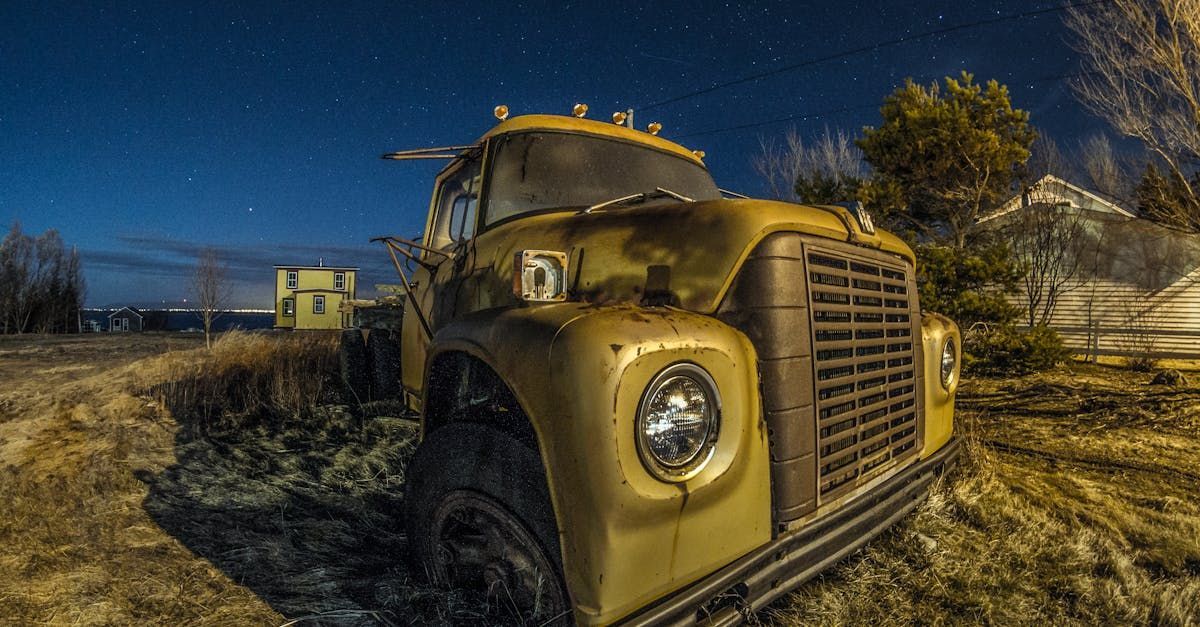 An old yellow truck is parked in a field at night.