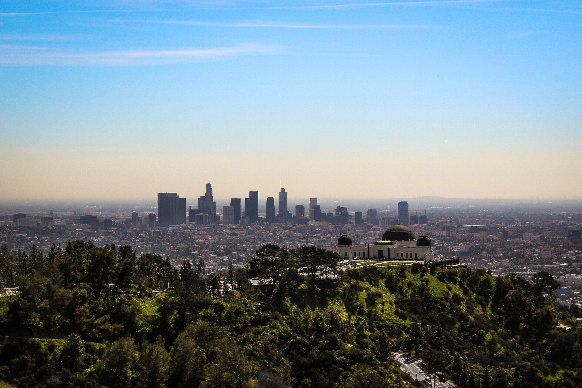 Los Angeles skyline with Griffith Observatory in the foreground, under a clear blue sky.
