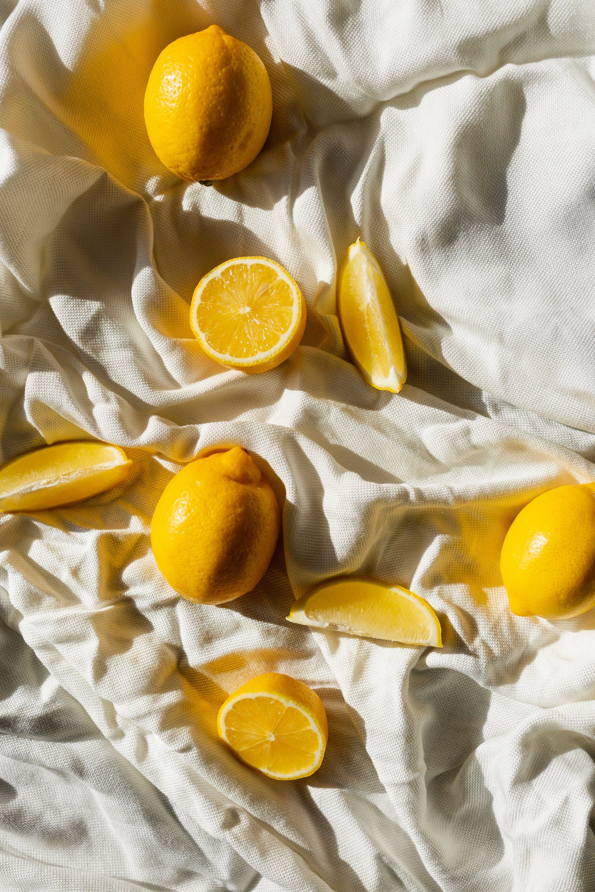 Bright yellow lemons and lemon slices scattered across a crumpled white fabric background.