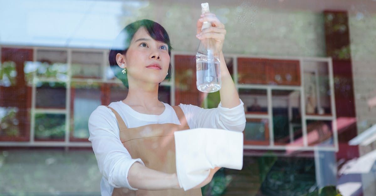 Woman holding up a water bottle in a bright indoor setting, with a towel draped over her arm.
