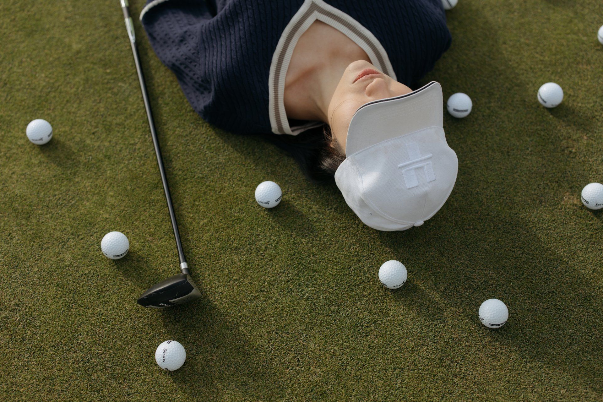A person is laying on a golf course surrounded by golf balls and a golf club.