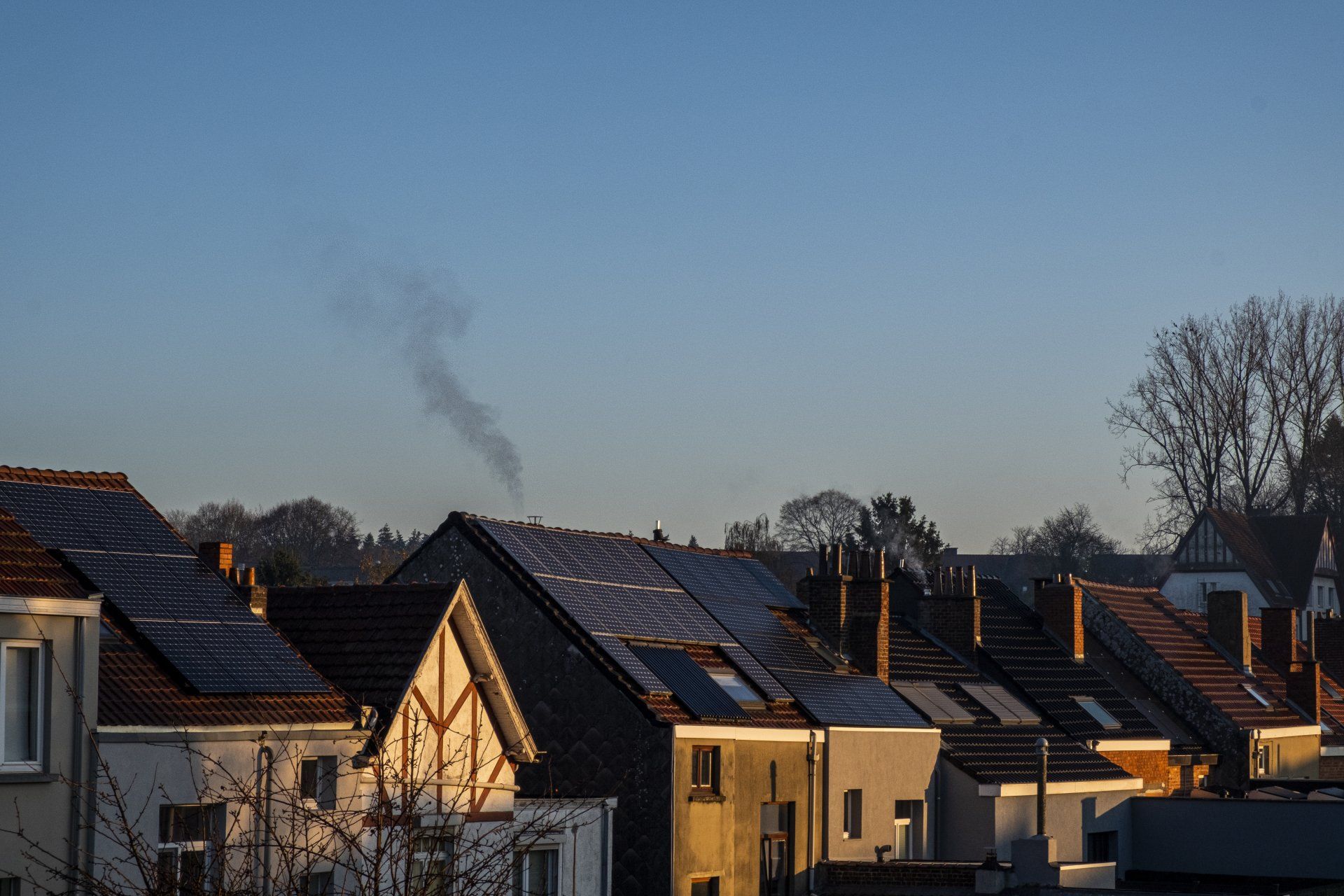 Een rij huizen met zonnepanelen op de daken en rook die uit de schoorstenen komt.