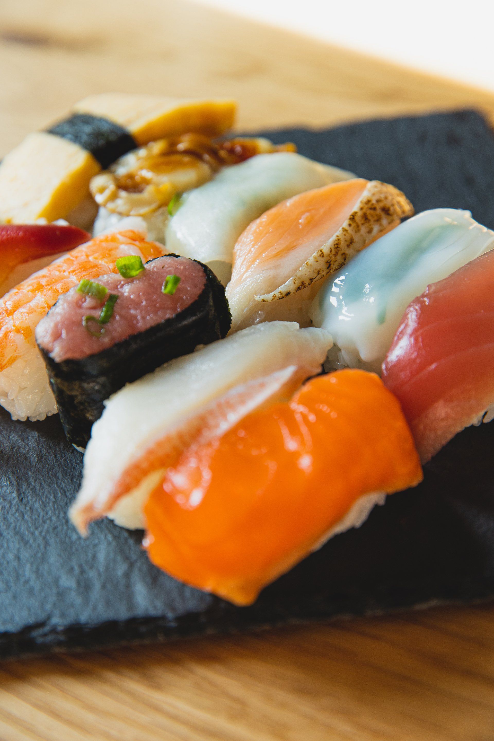 Sushi nigiri assortment on a dark stone plate. Variety of seafood, rice, and nori.
