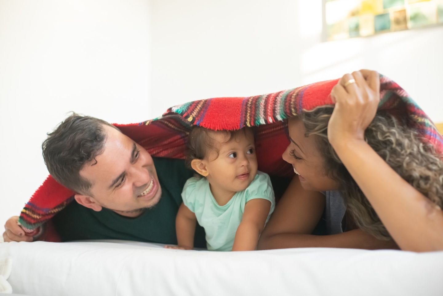A man and woman are laying on a bed with a baby under a blanket.