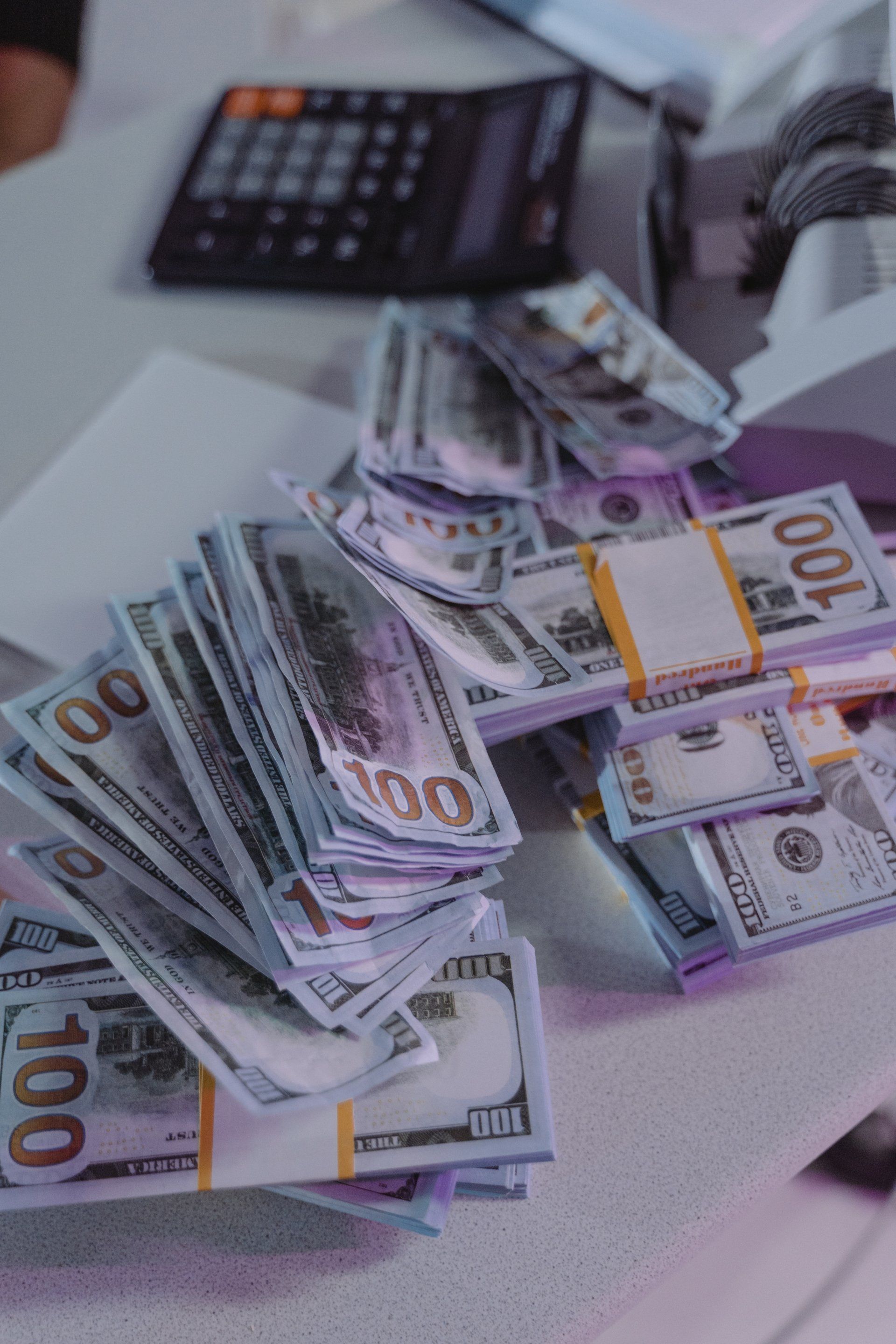 A pile of money is sitting on a table next to a calculator.