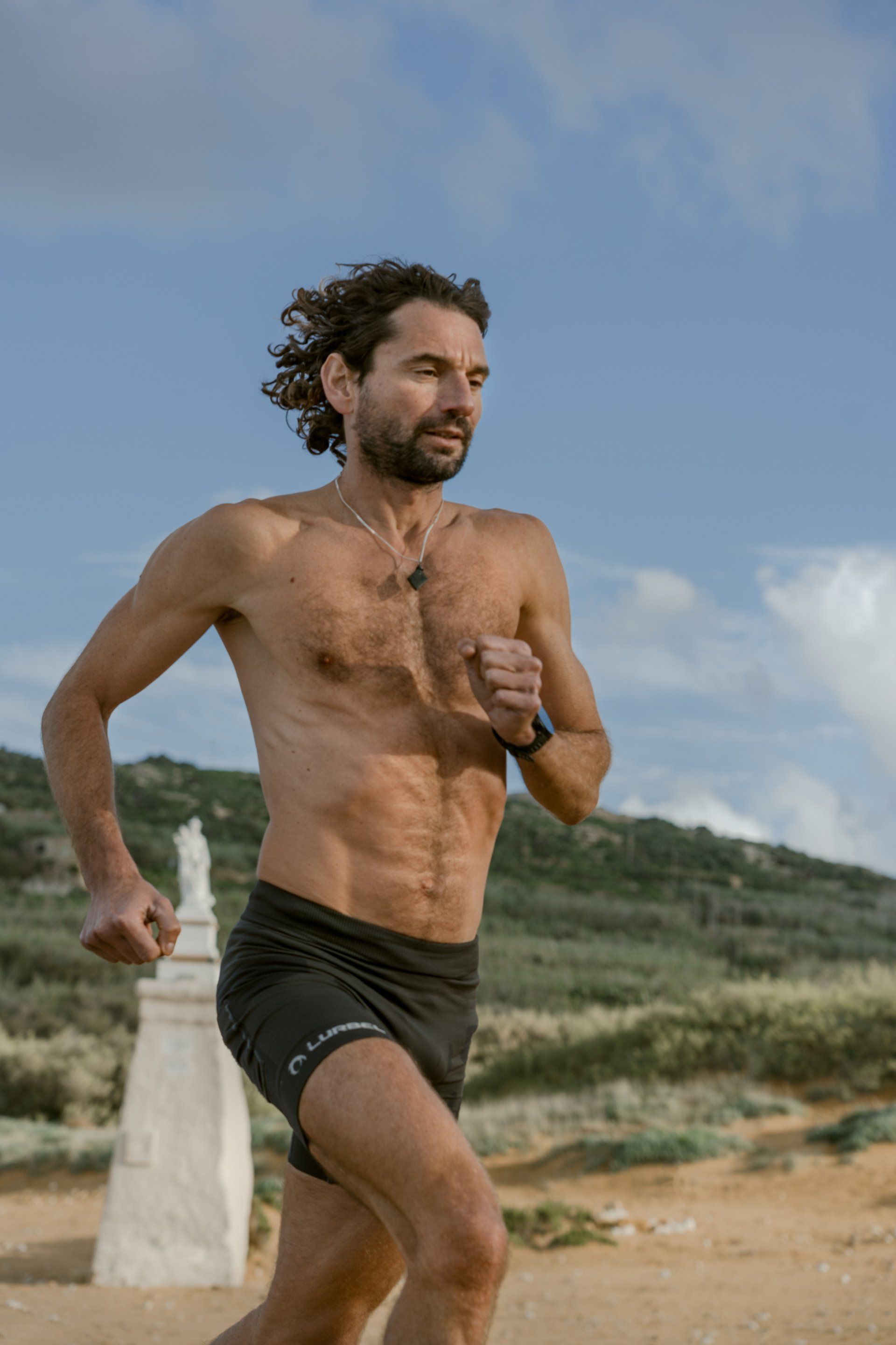 A shirtless man is running on a dirt road.