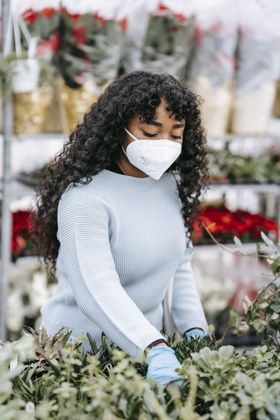 A woman wearing a mask and gloves is picking flowers in a garden.