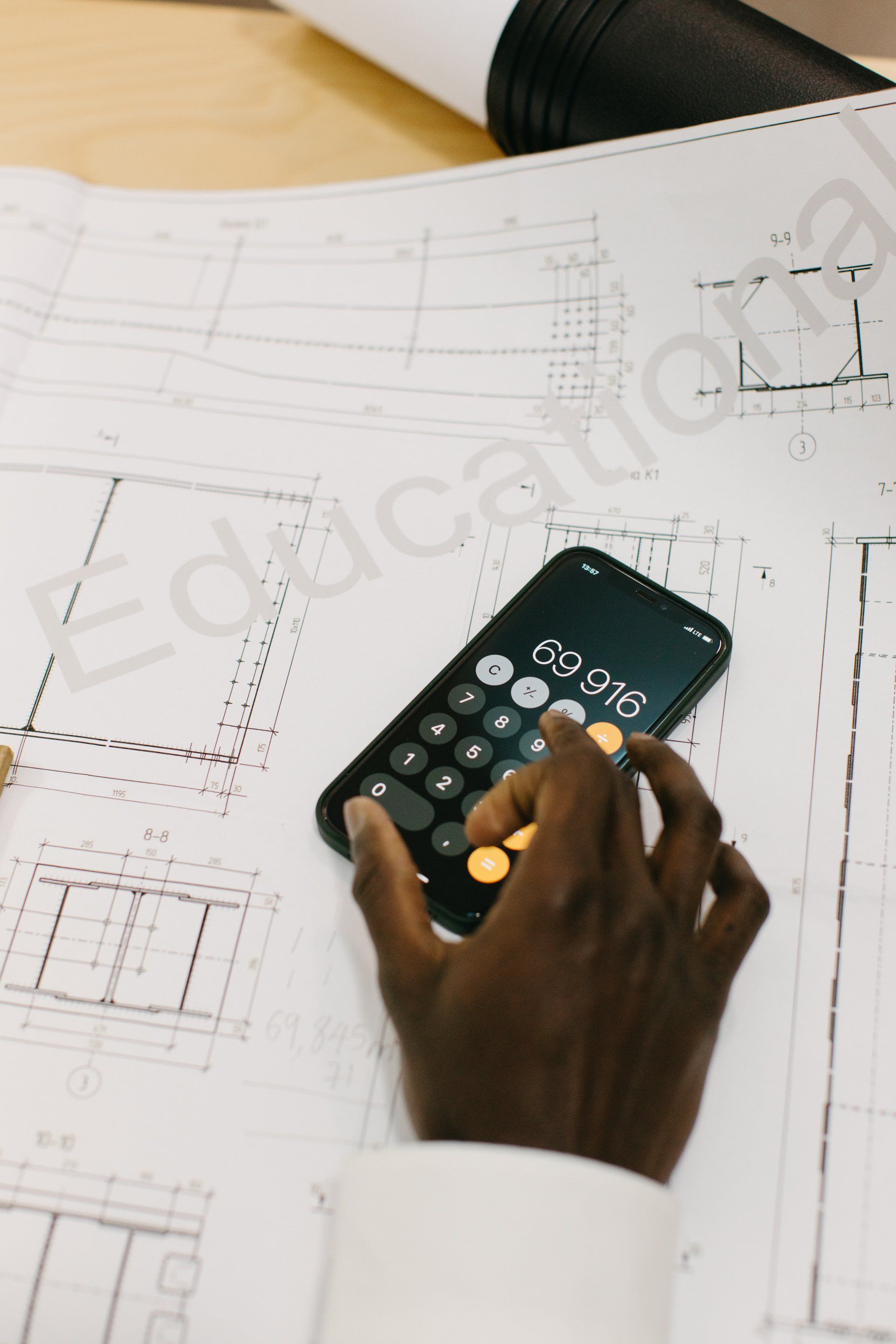 Person's hand using a calculator on top of architectural blueprints.