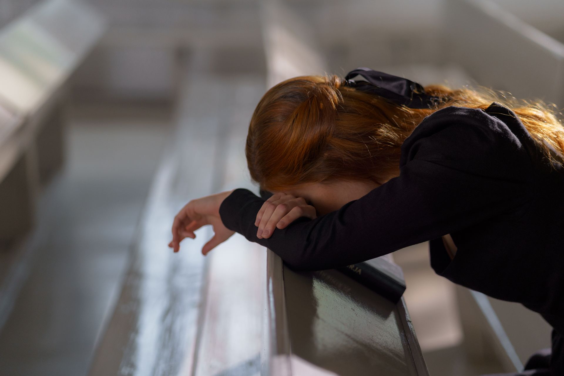 A woman is leaning on a railing with her head down.