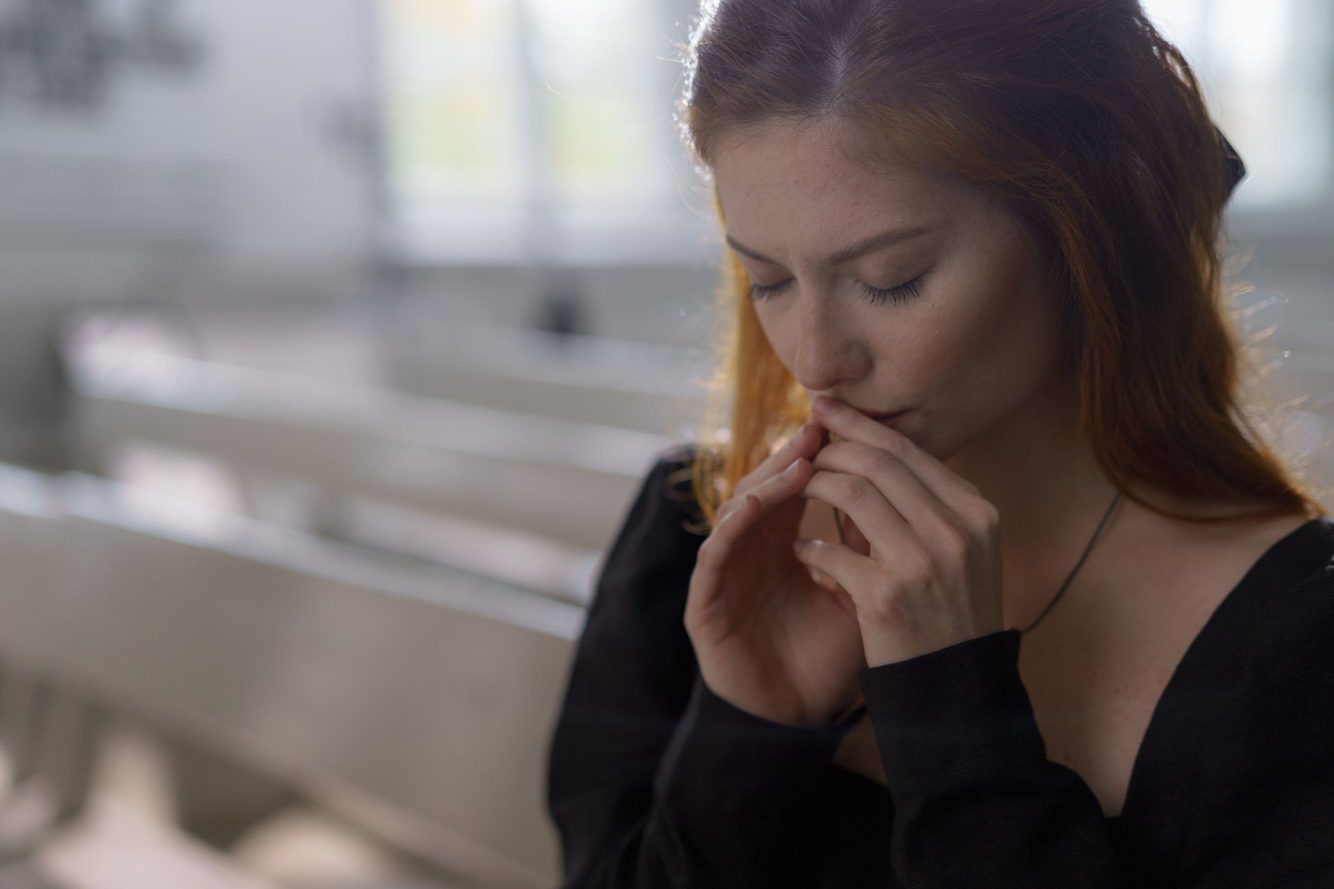 A woman is sitting on a couch covering her mouth with her hands.