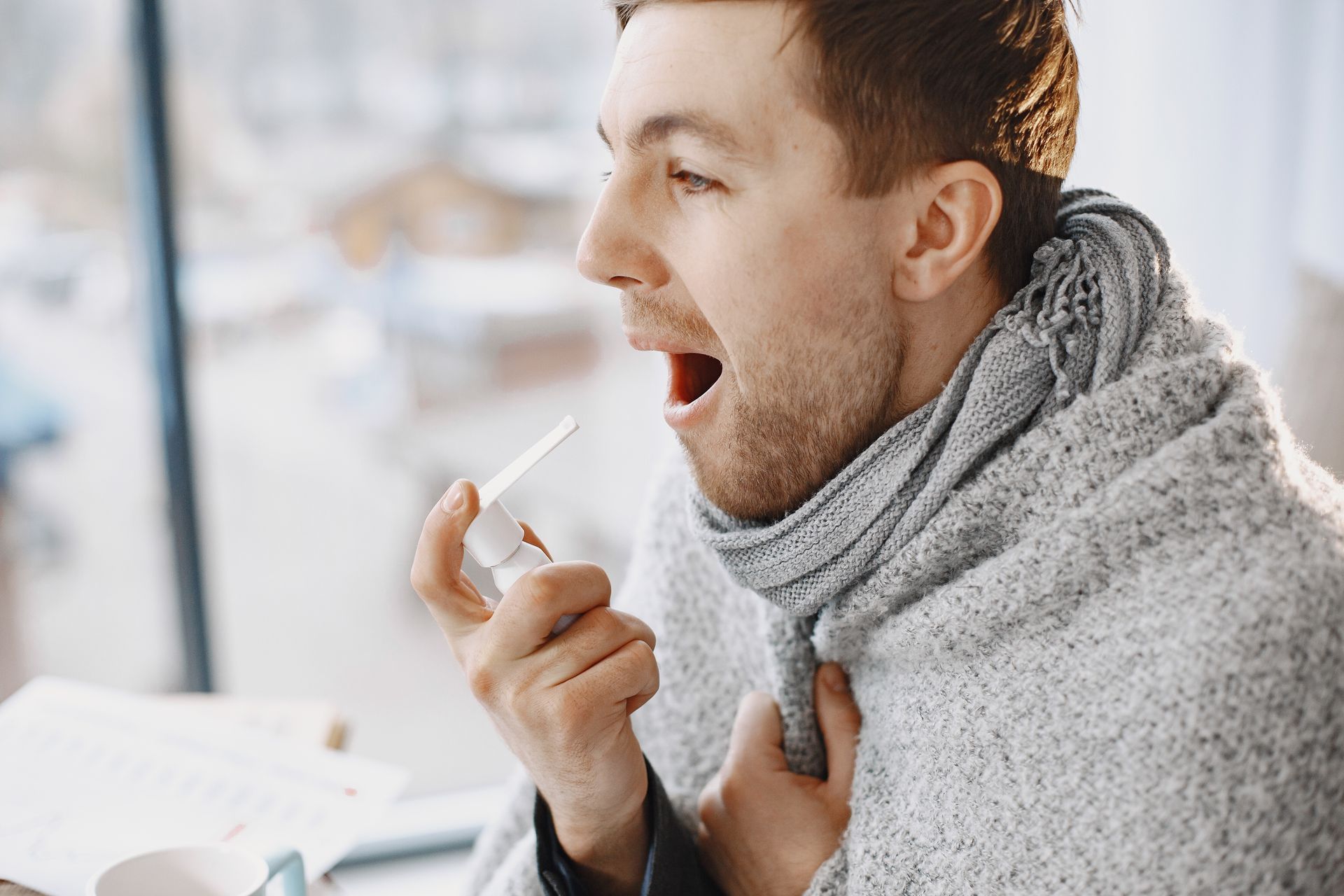 man using an oral spray for a sore throat