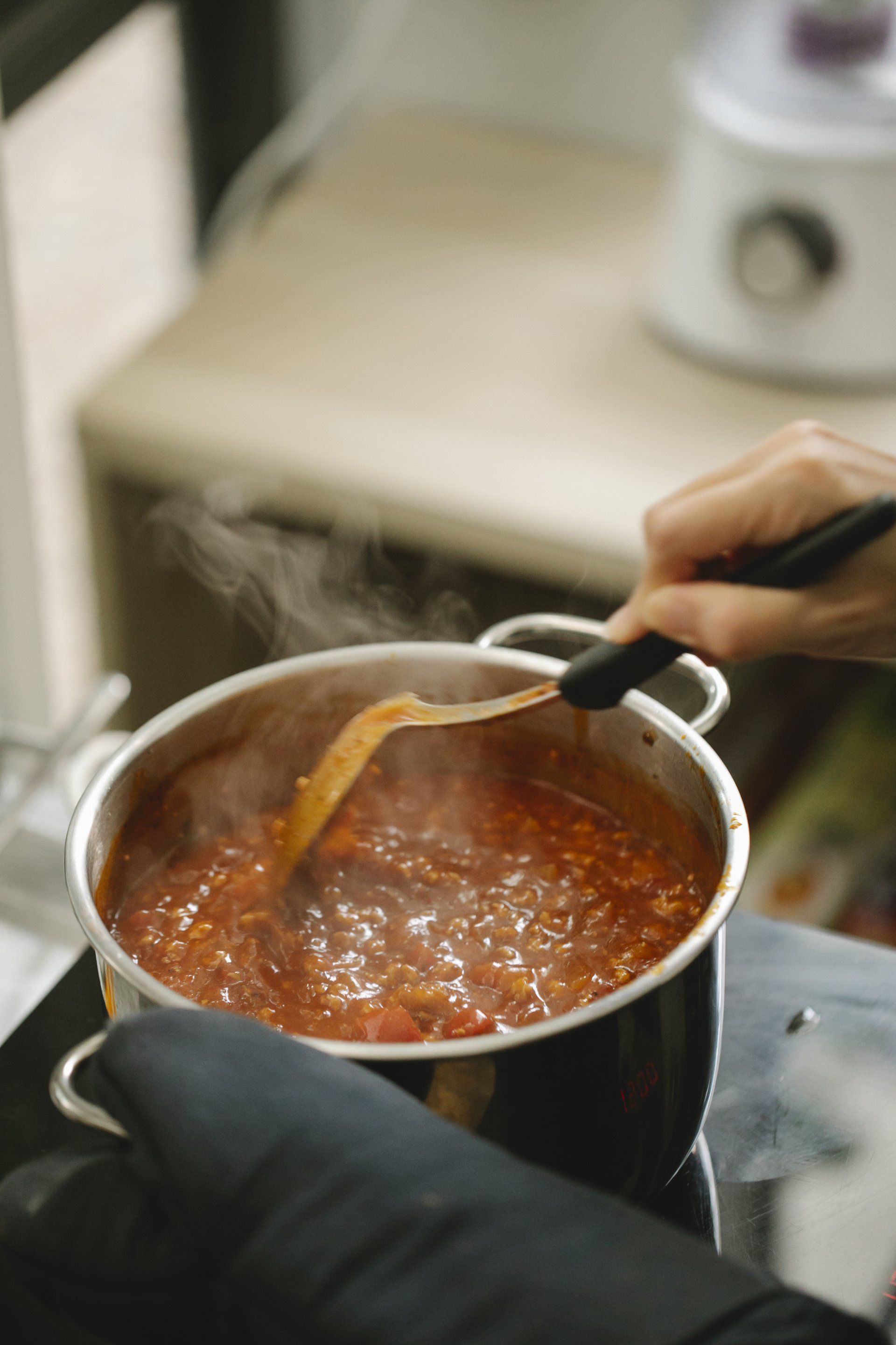 Hand stirring a pot of red sauce on a stovetop with a spoon