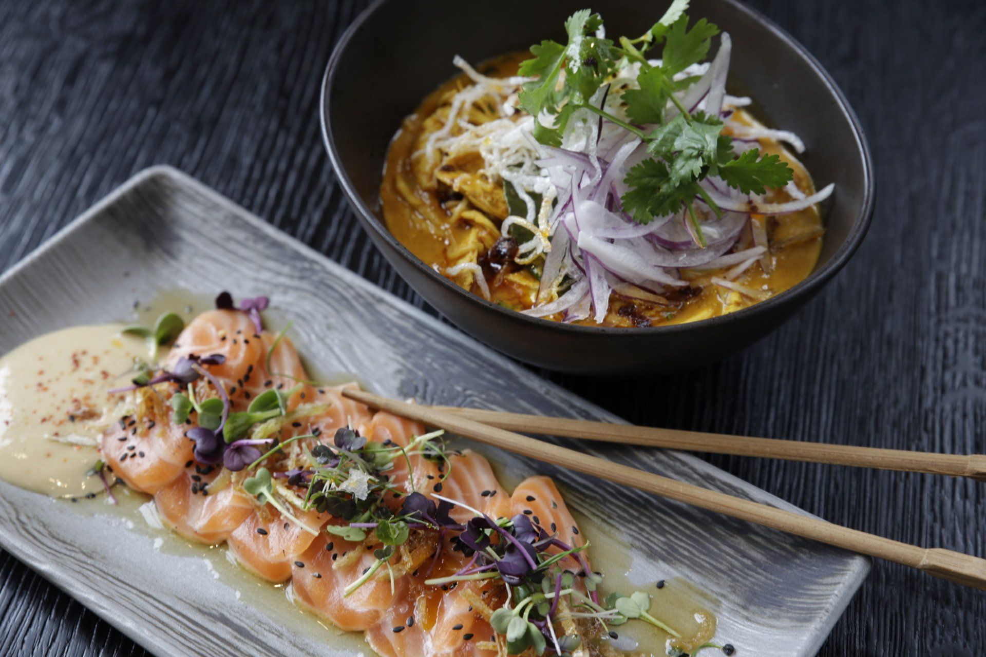 A plate of food with chopsticks next to a bowl of food on a table.