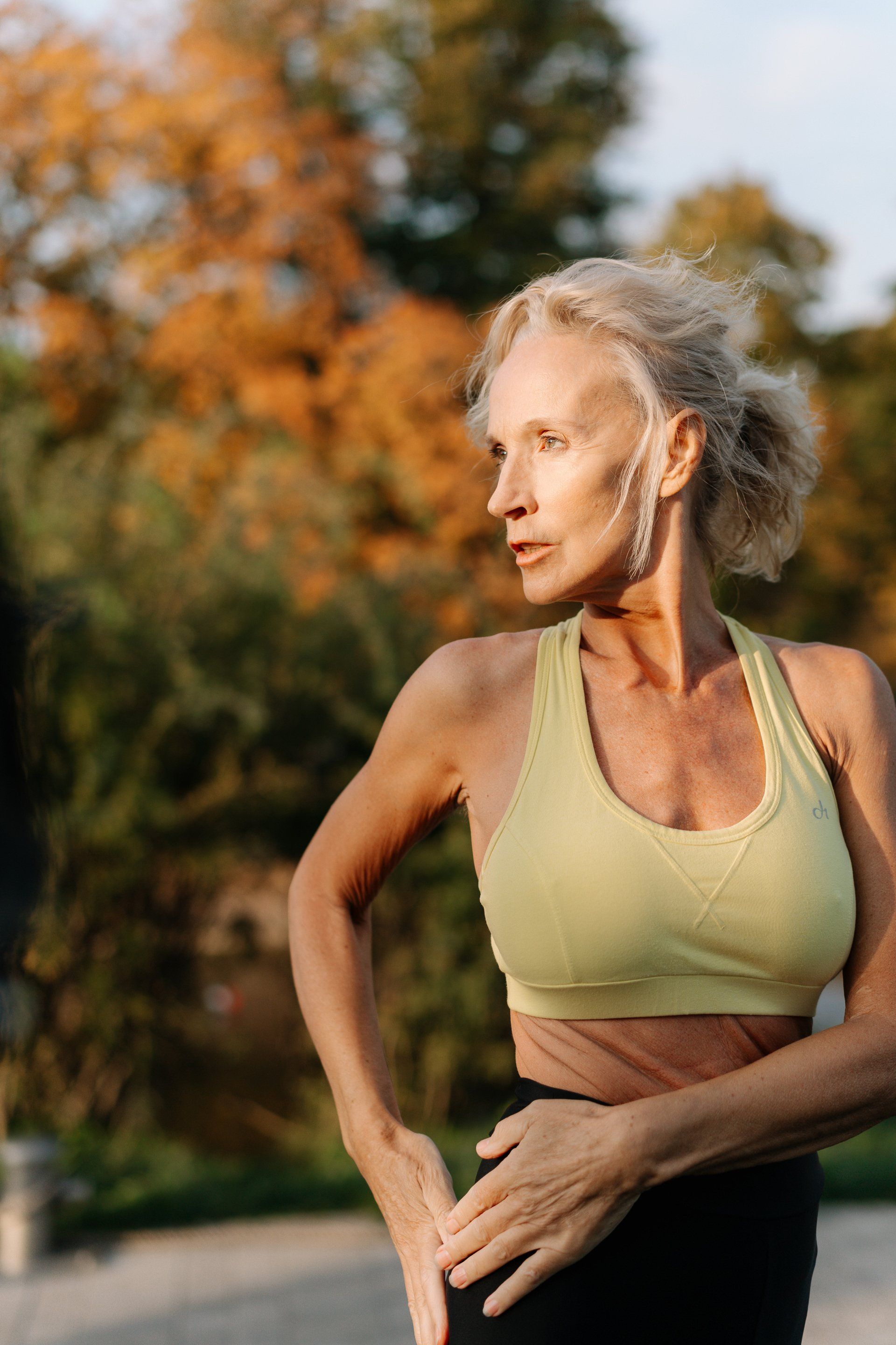 An older woman in a sports bra is standing in a park.