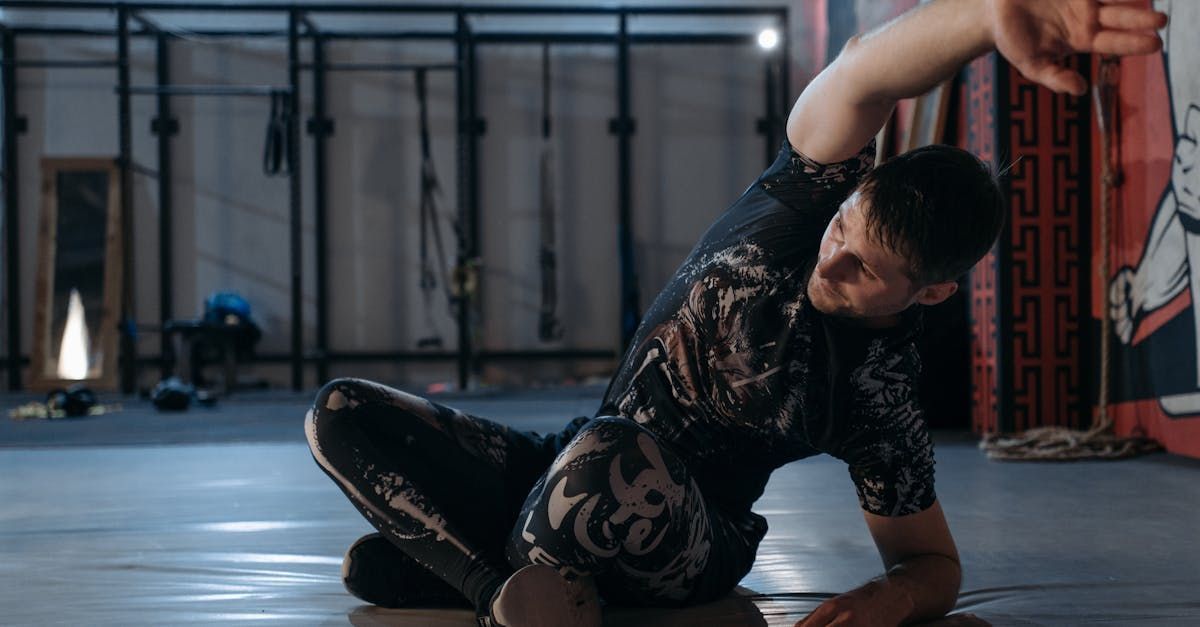 A man is kneeling on the floor in a gym stretching his arms.