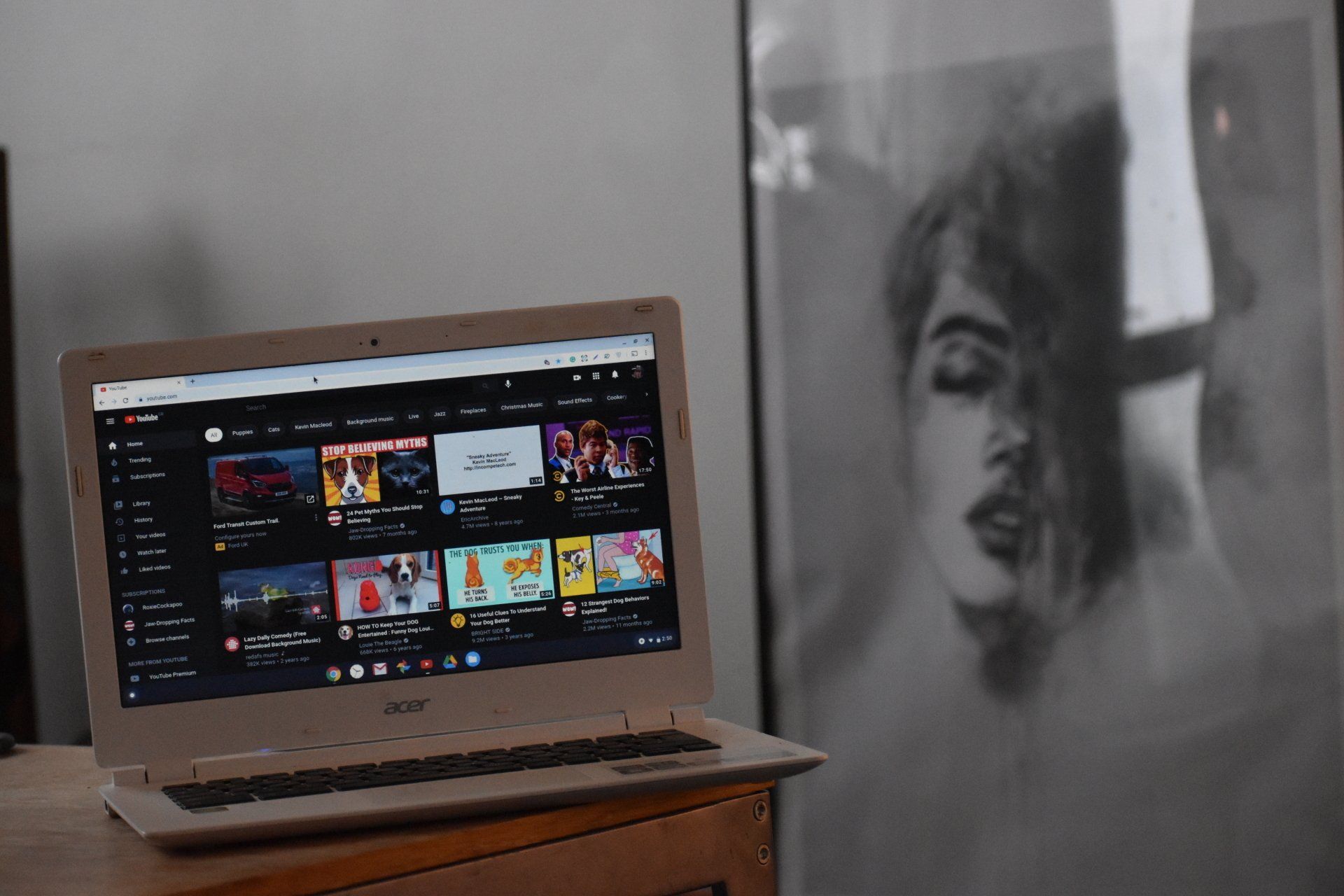 A laptop computer is sitting on a table next to a painting of a woman.