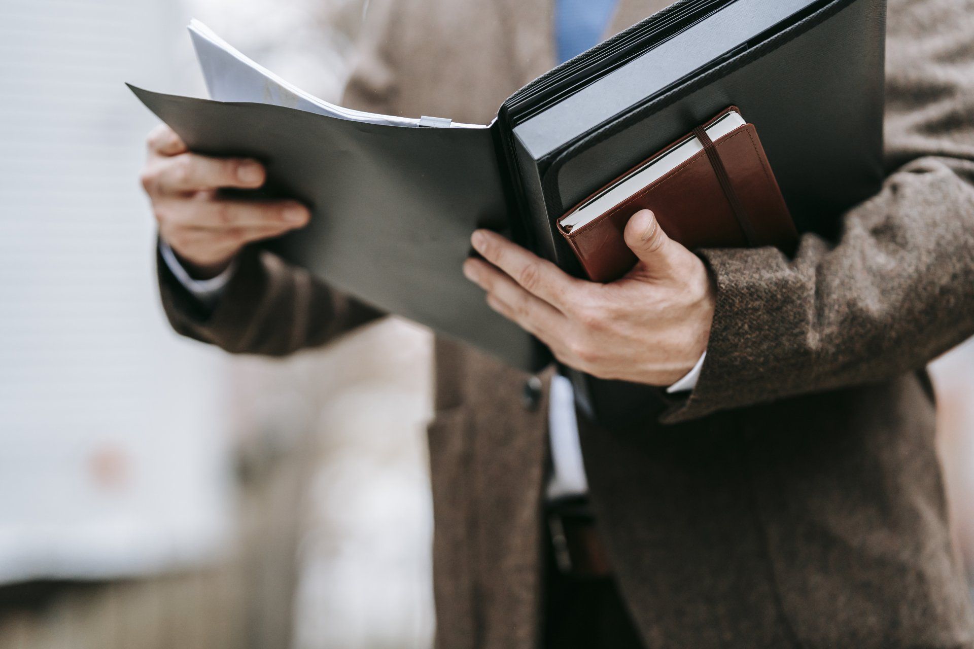 Person in brown blazer holding a file folder, binder, and notebook.