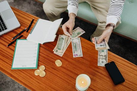 A person is sitting on a couch counting money on a table.
