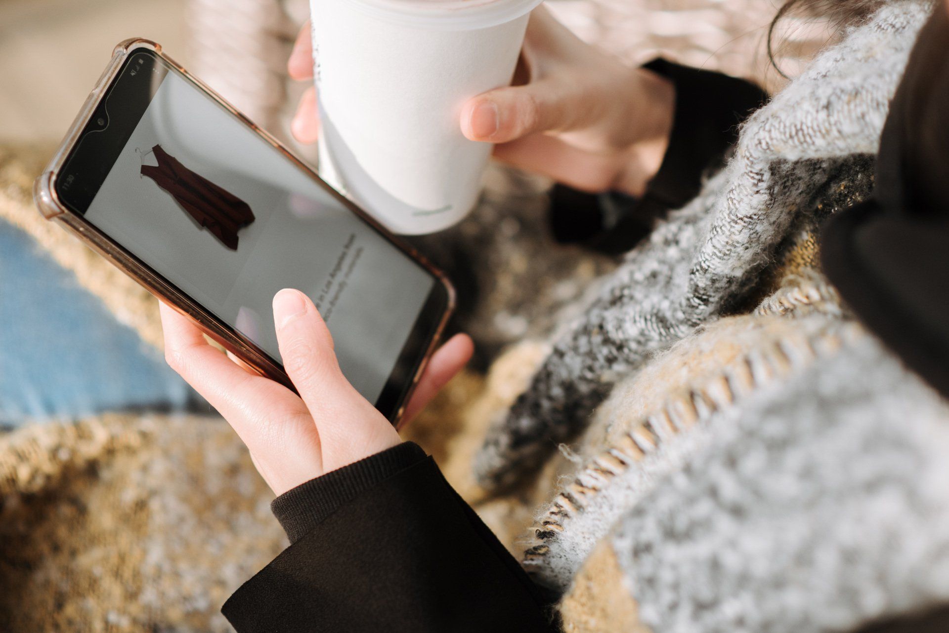 a woman is holding a cup of coffee and shopping on her phone