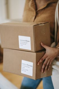 Person carrying two stacked cardboard boxes in a doorway