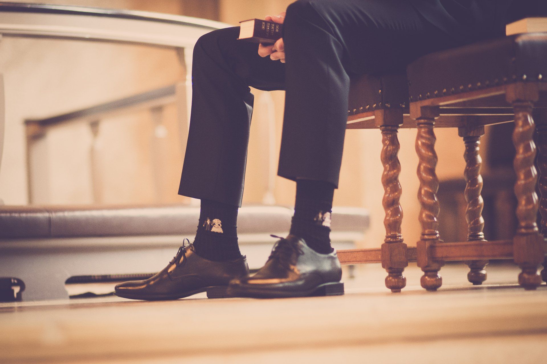 A man is sitting on a wooden chair with his legs crossed.