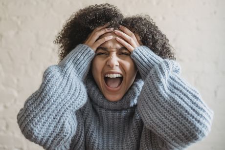 A woman in a sweater is screaming with her mouth open.