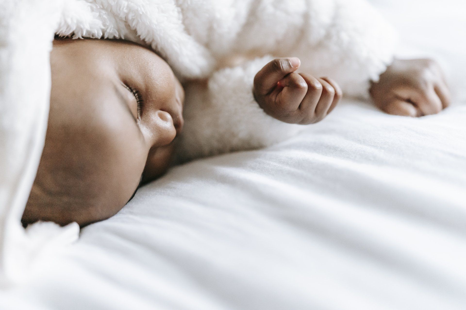 A baby peacefully sleeping on a soft white blanket, resting comfortably.