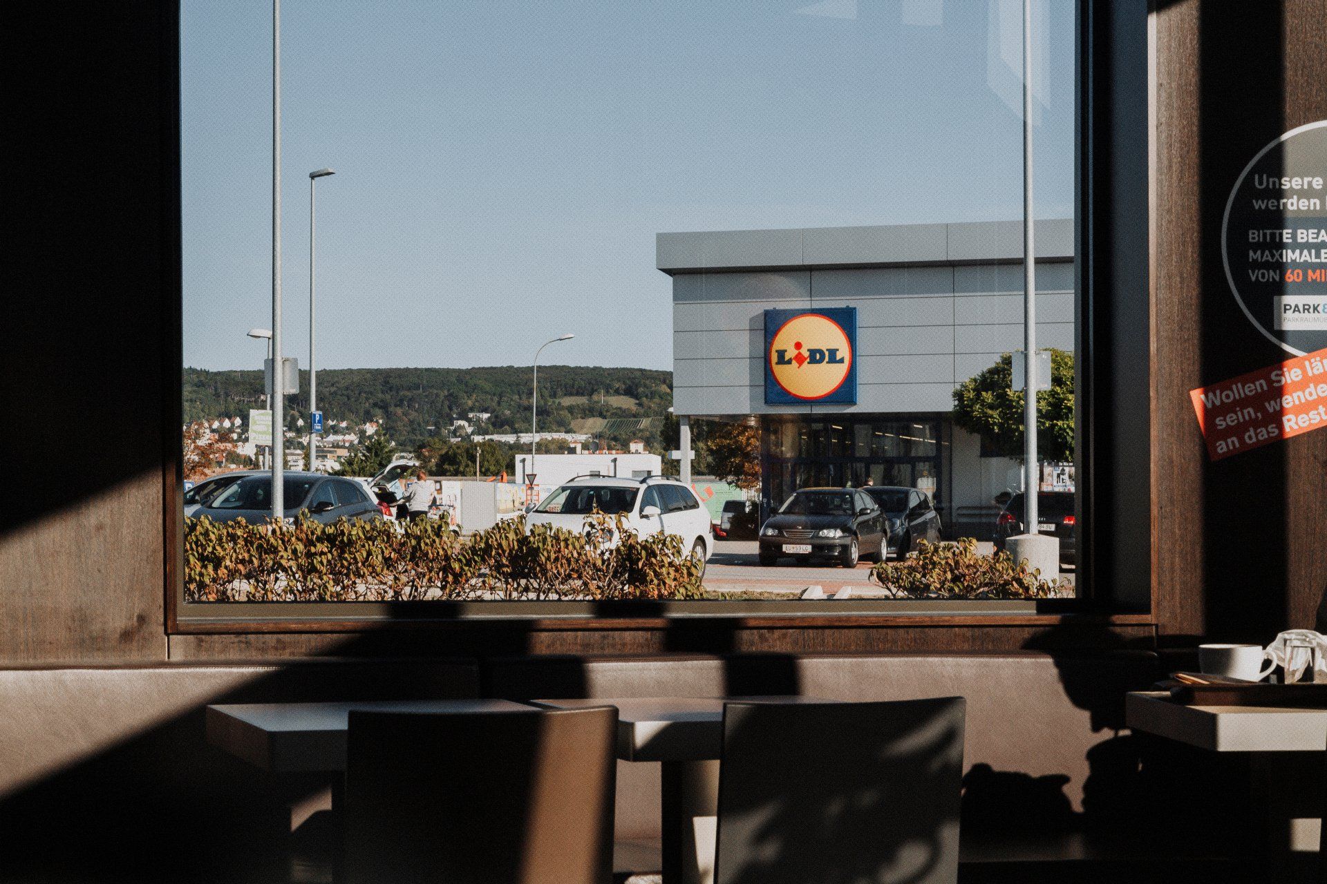View of a Lidl supermarket from a window, with cars in a parking lot on a sunny day.
