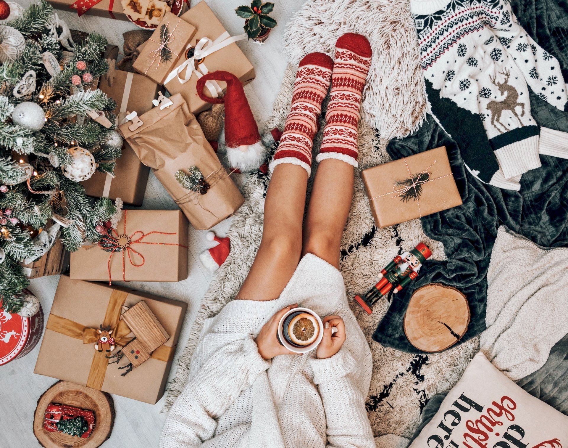 Una donna è sdraiata sul pavimento con una tazza di caffè davanti a un albero di Natale.