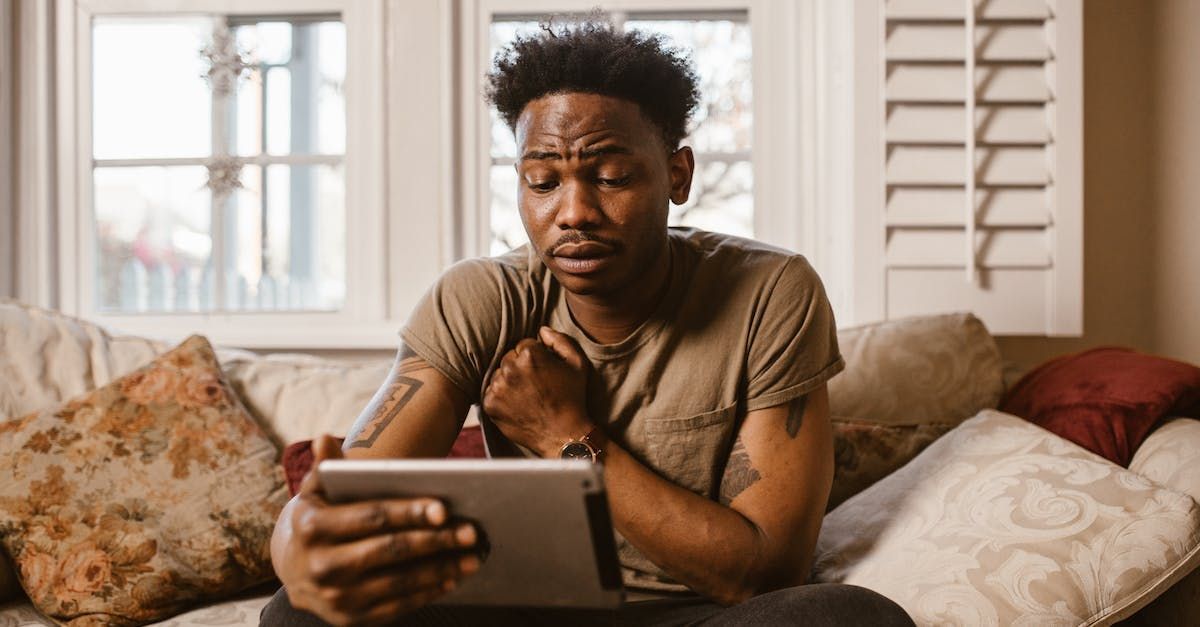 A man is sitting on a couch using a tablet computer.