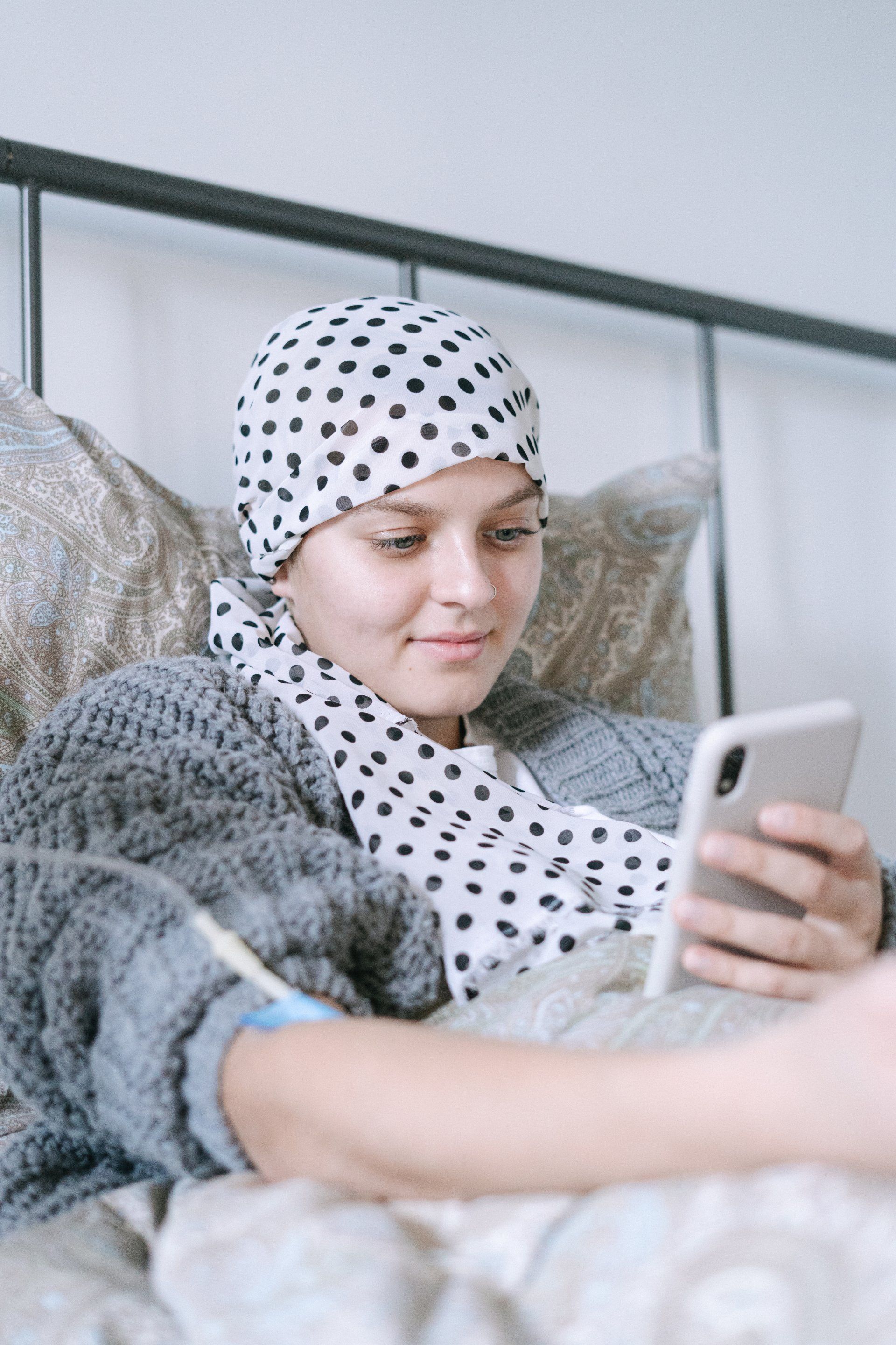 A woman with cancer is laying in bed looking at her cell phone.