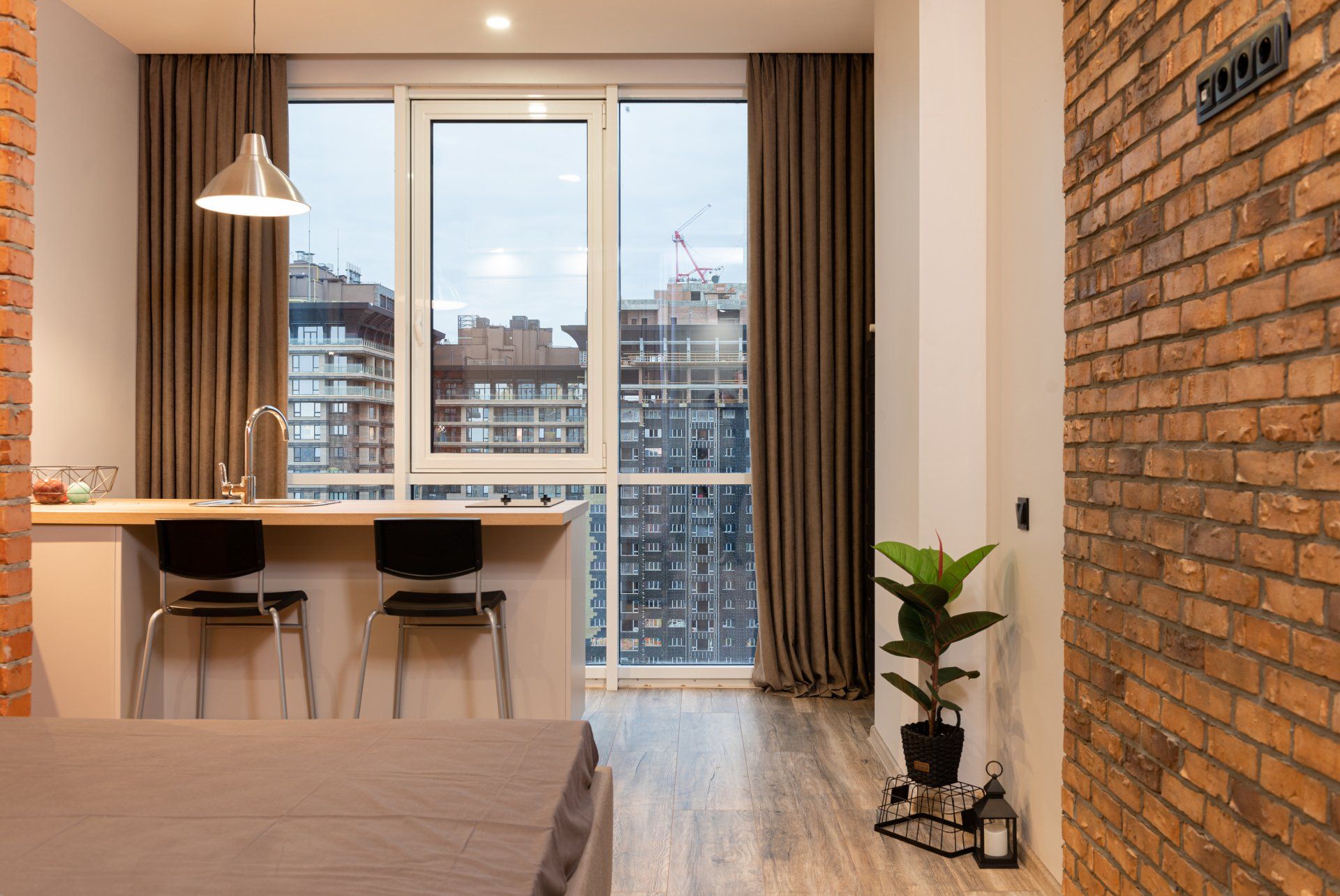 a living room with a large window, a kitchen, and a brick wall
