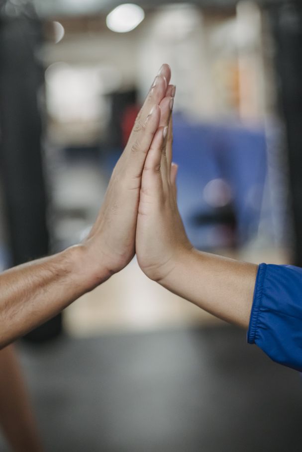 Two people join hands in a vertical high-five gesture in an indoor setting.
