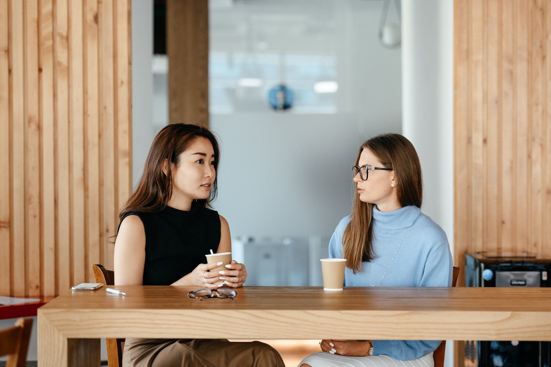 Two women are sitting at a table talking to each other.