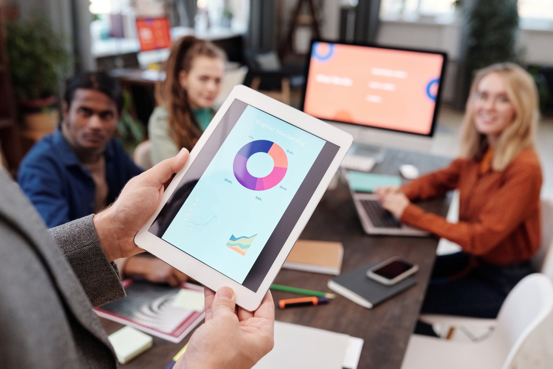 Person holding tablet with charts, presenting to a group in an office.