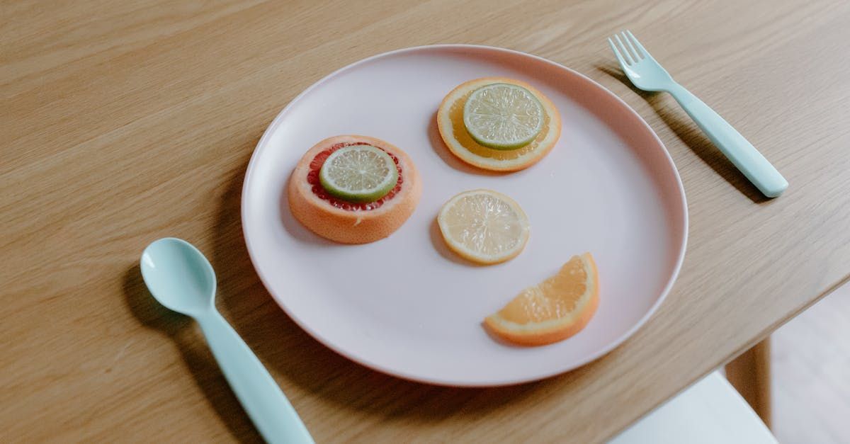 A pink plate topped with fruit slices and a fork and spoon on a wooden table.