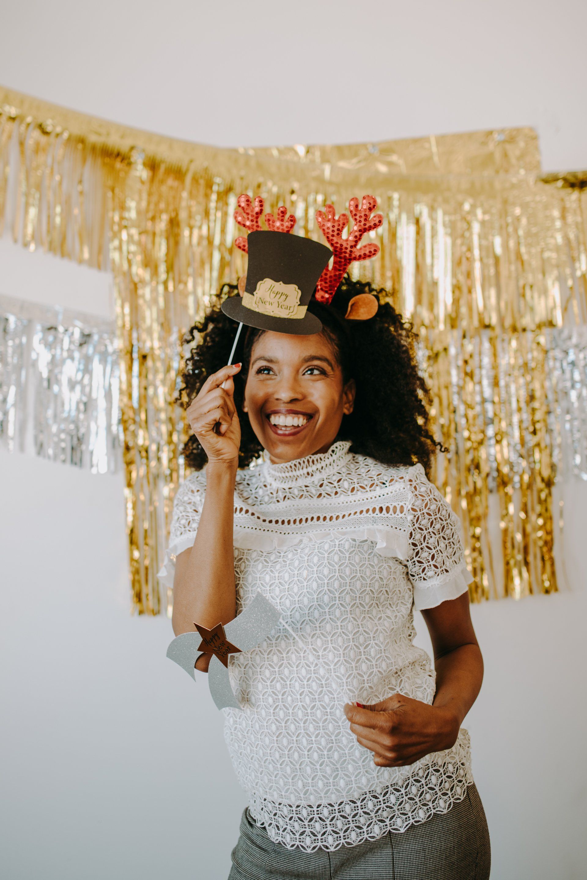 A woman wearing a top hat and reindeer antlers is holding a photo booth prop.
