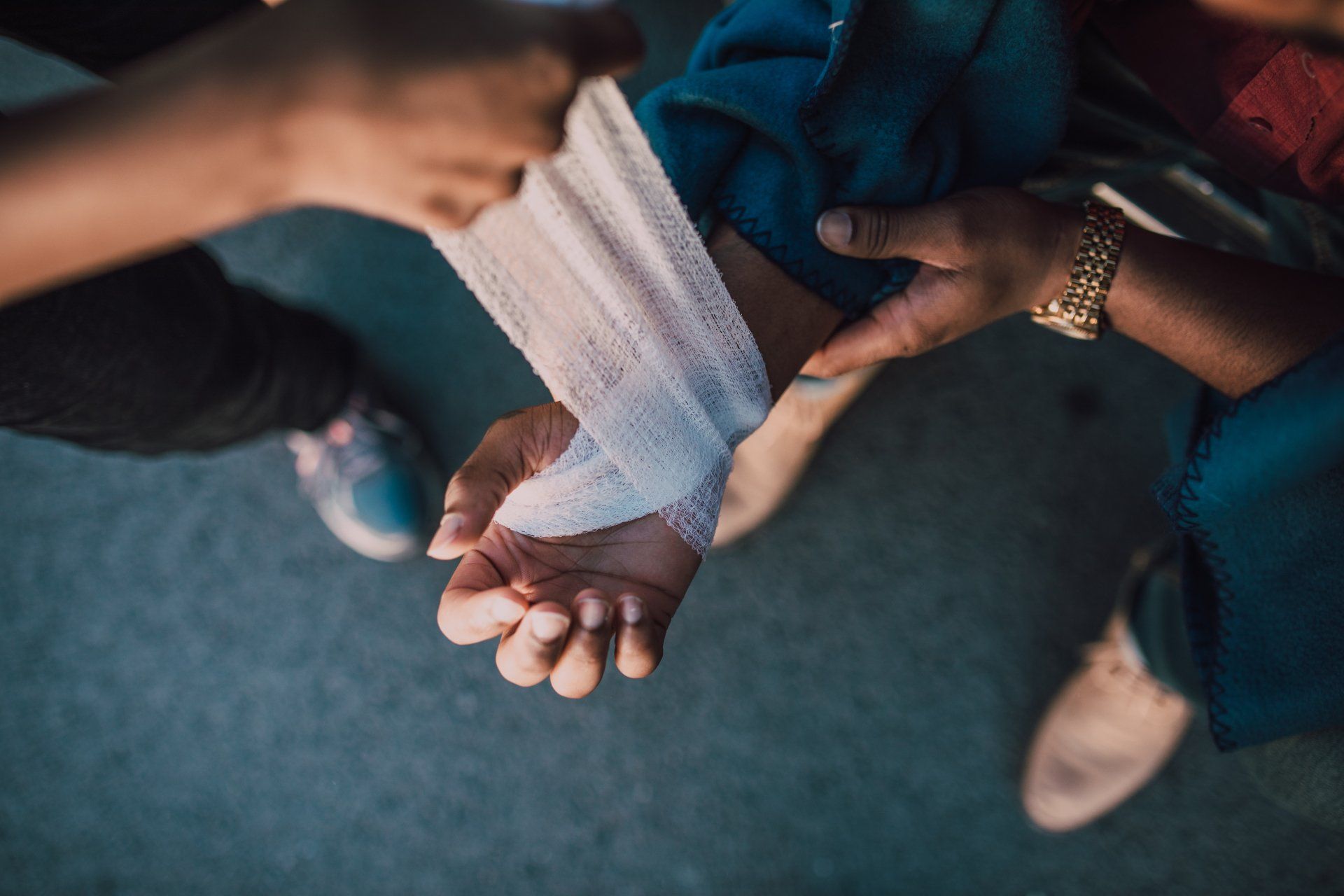 A person's arm being bandaged by another person's hands, close up. Both are wearing dark clothing.