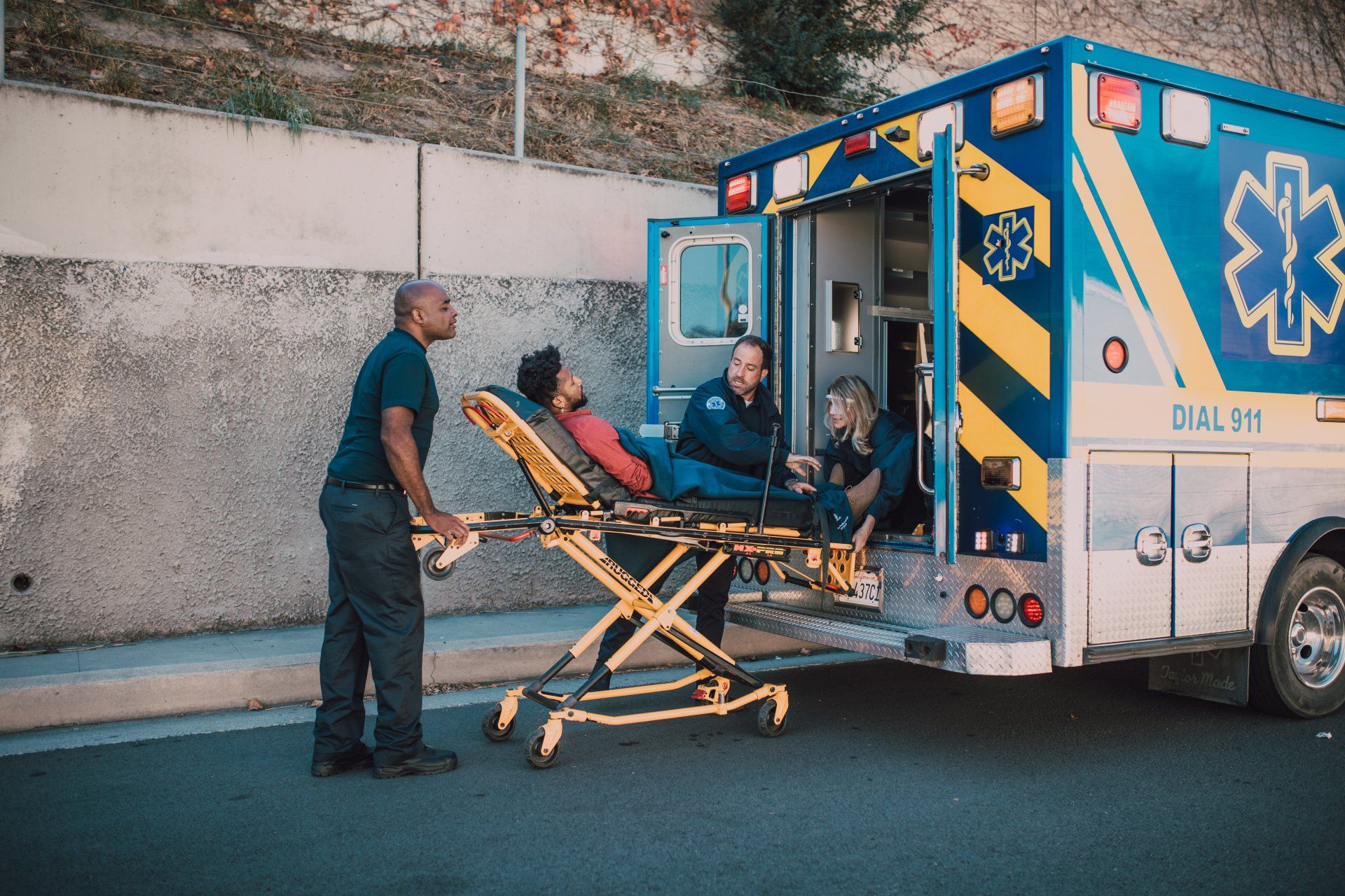 Paramedics loading a patient on a stretcher into an ambulance outside a building