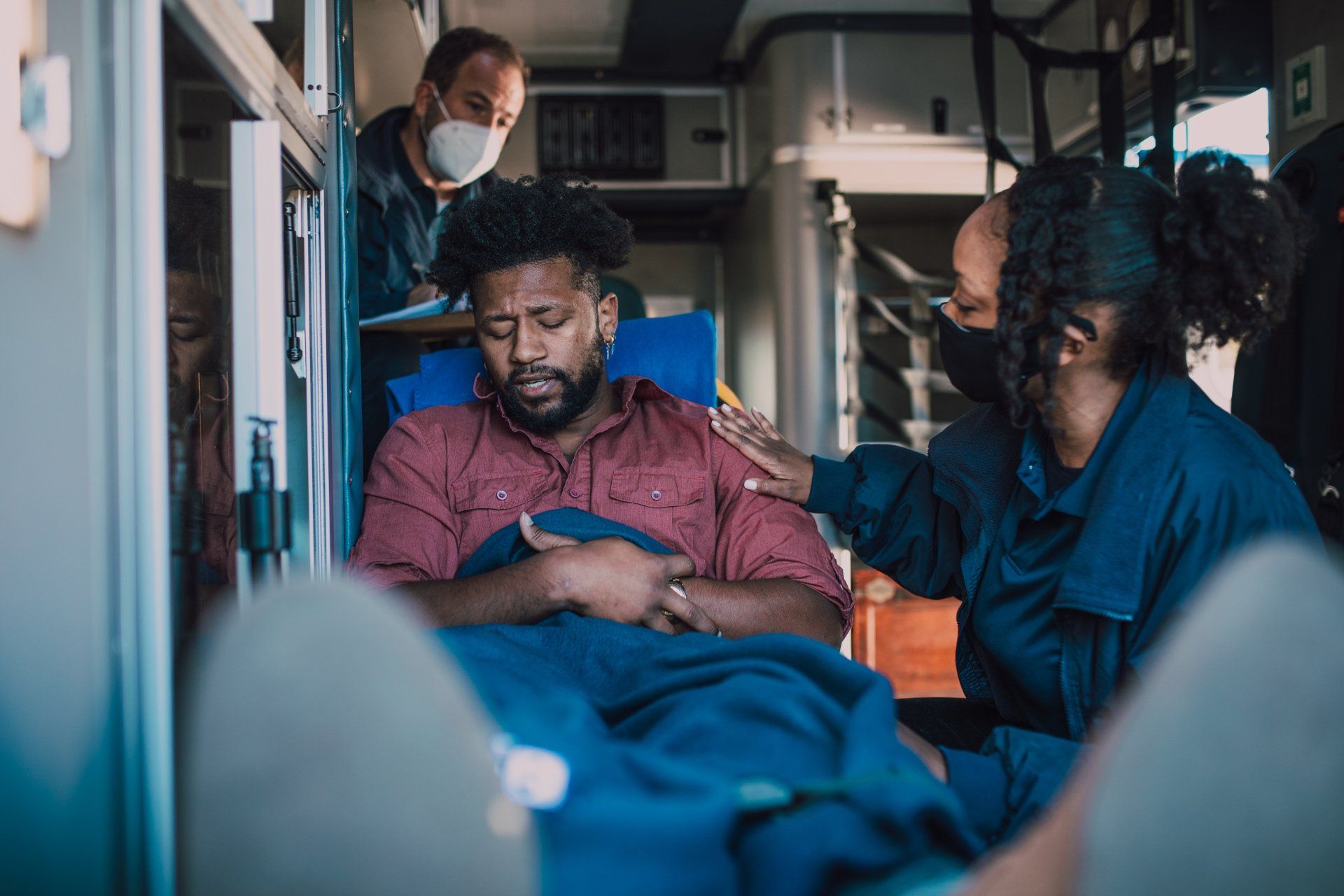 Two nurses care for a man lying on a stretcher inside an ambulance