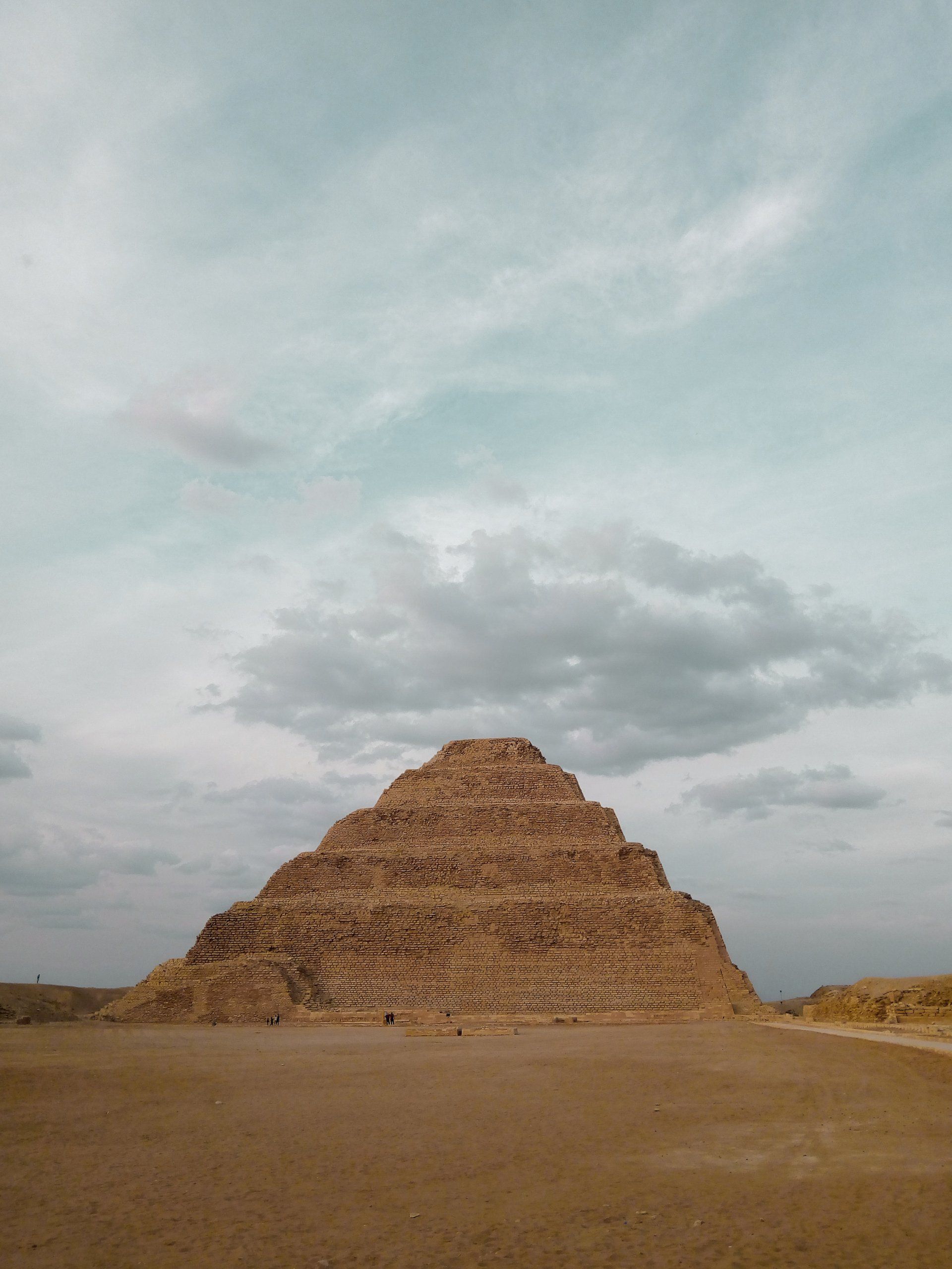 Step pyramid in a desert landscape under a cloudy sky.