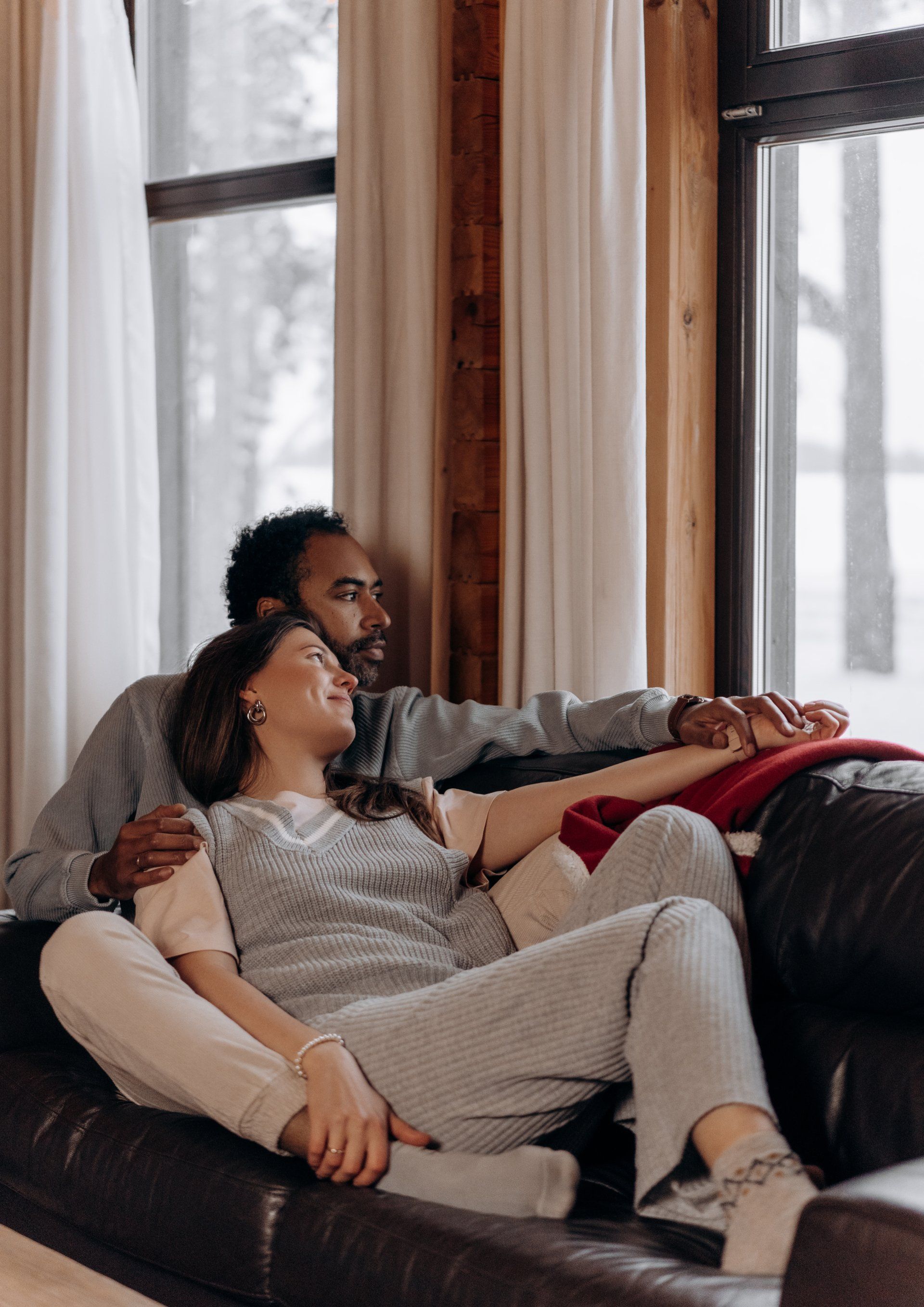 A man and a woman are sitting on a couch in front of a window.