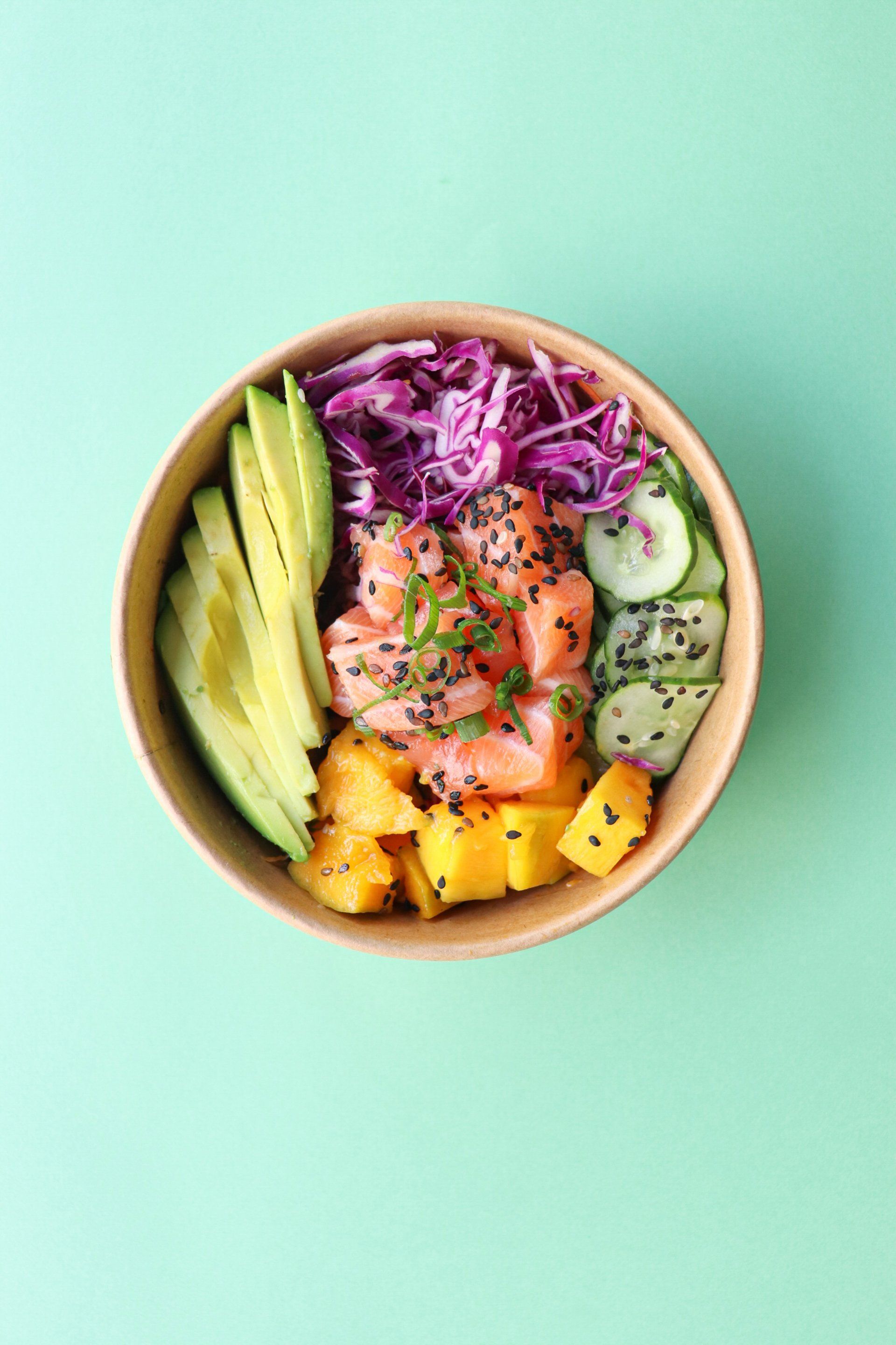 een kom poke met zalm, avocado, komkommers en kool op een groene achtergrond.