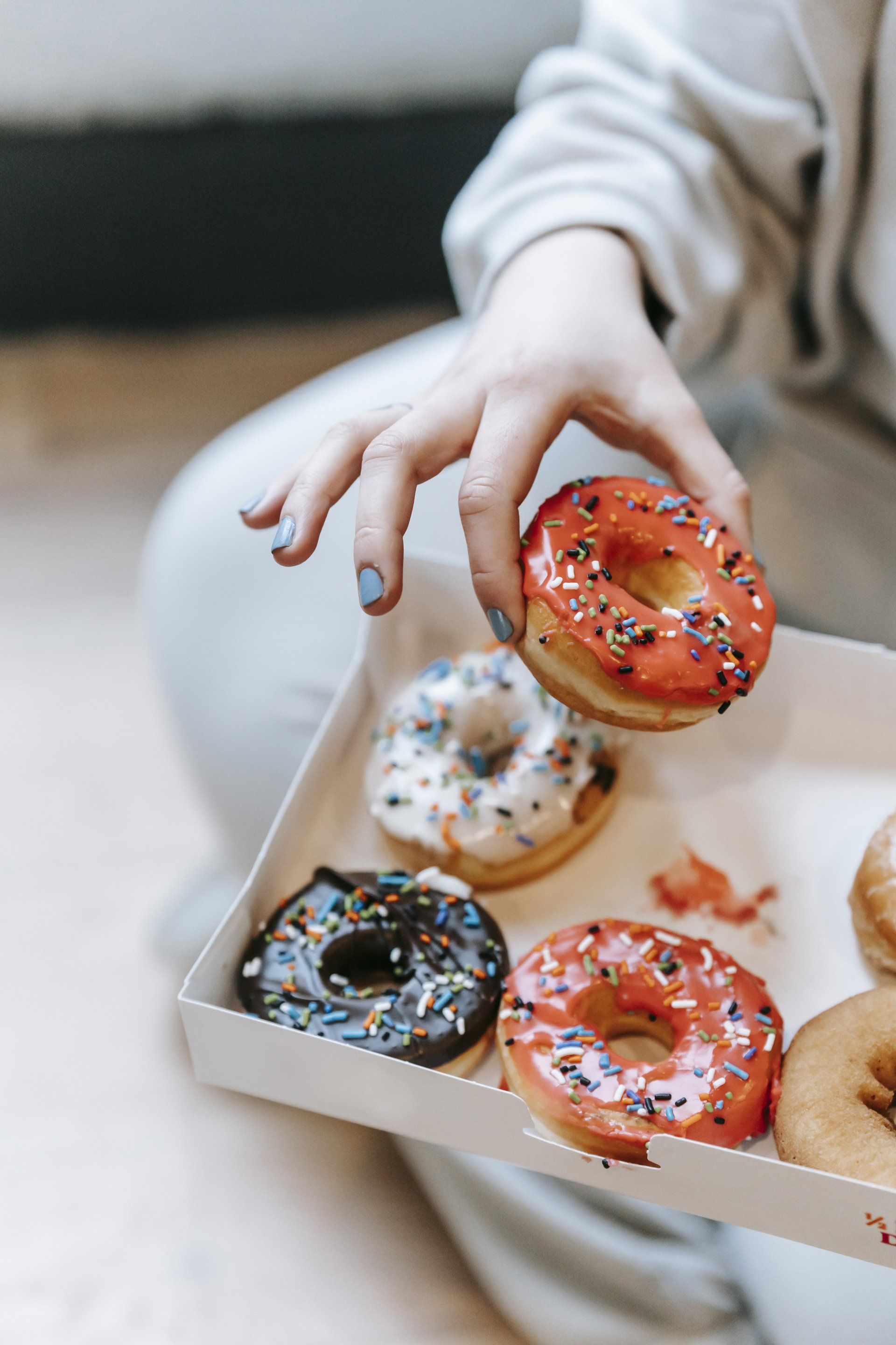 A person is taking a donut out of a box of donuts.