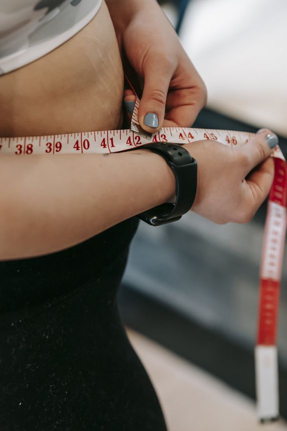 A woman is measuring her waist with a tape measure.
