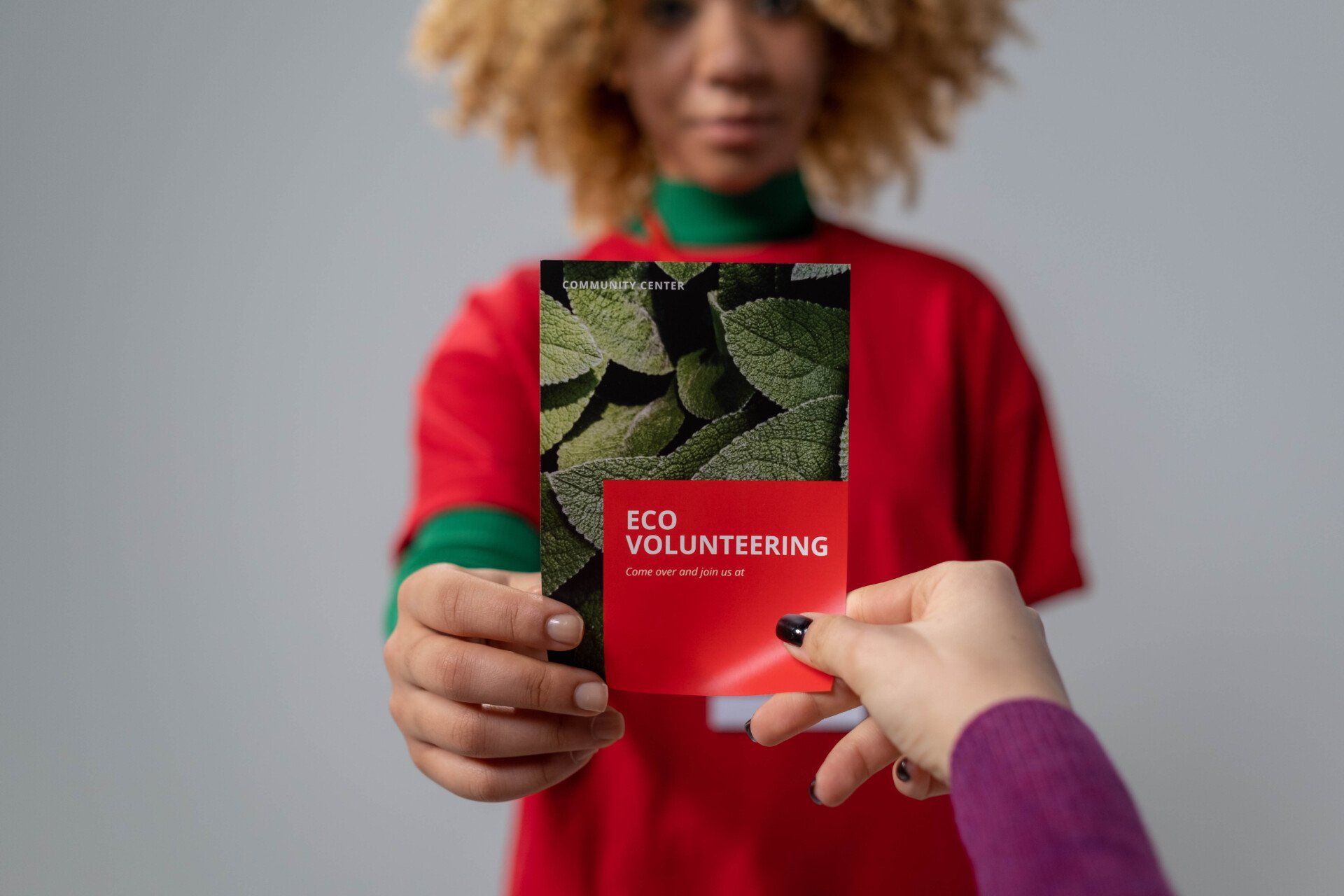 A woman in a red shirt is giving a flyer to another person.