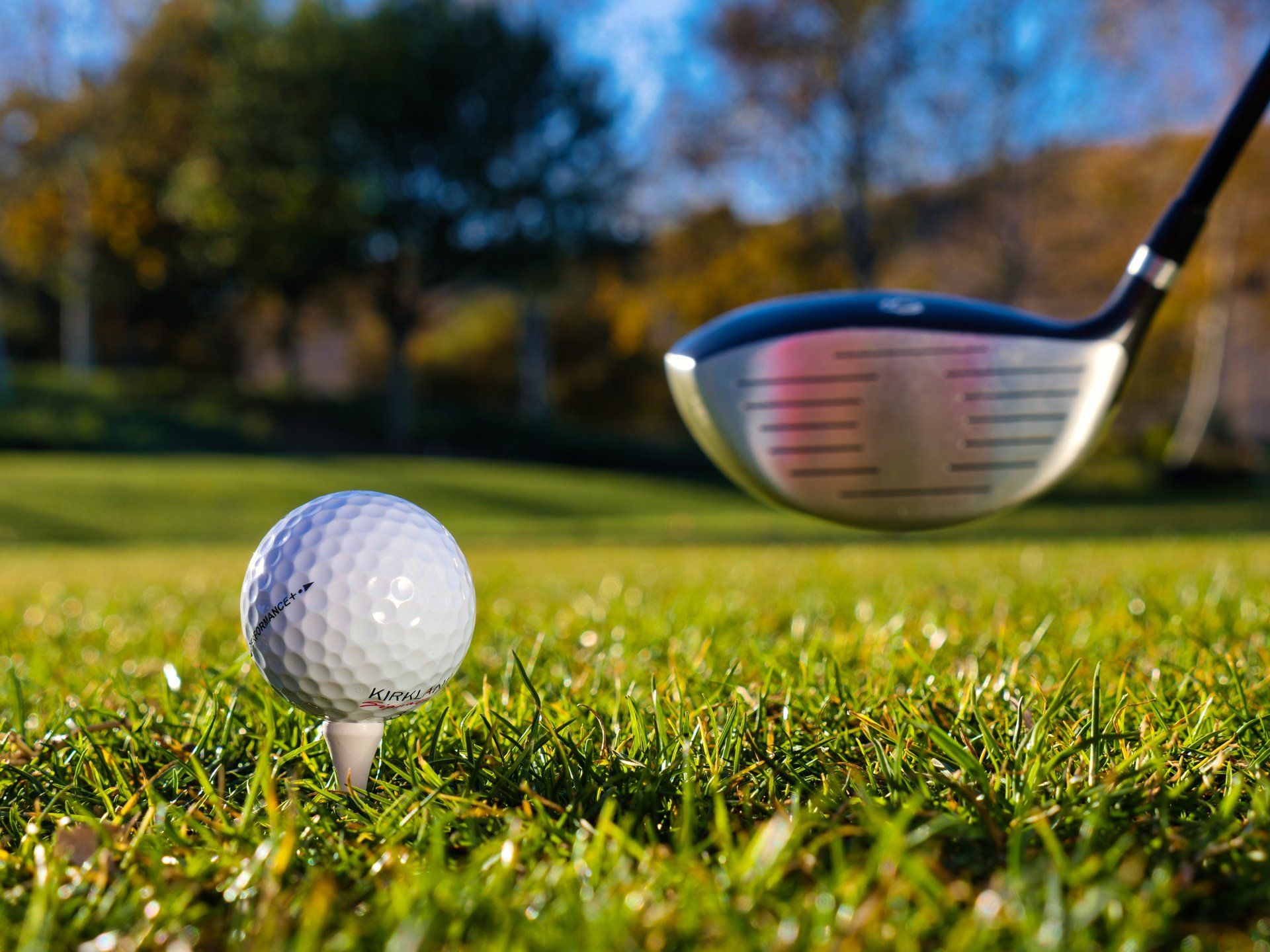 A golf ball is on a tee with a golf club in the background.