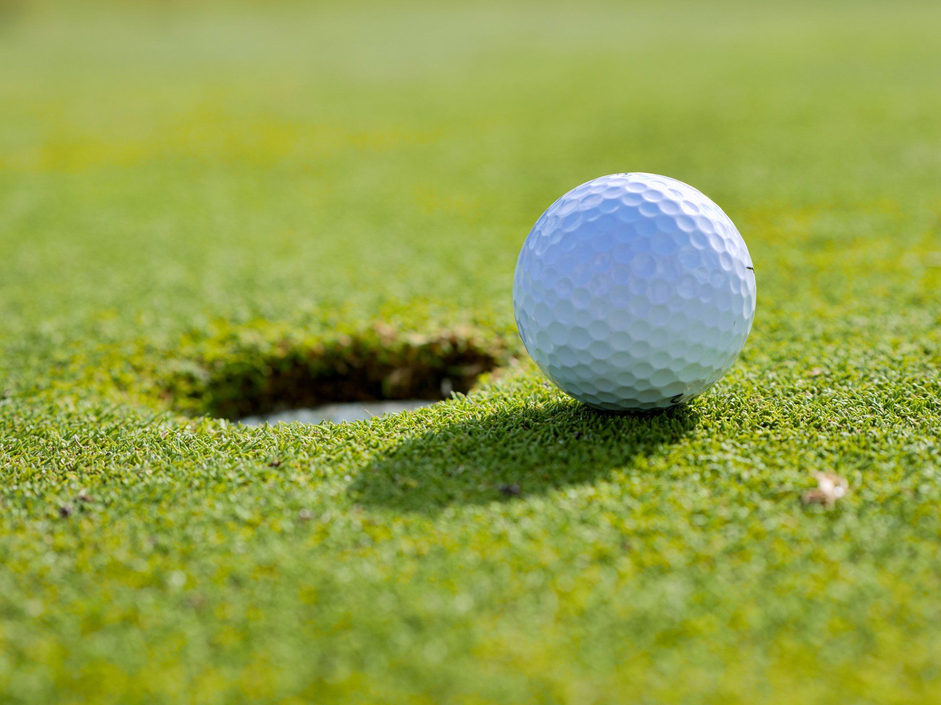 A golf ball is sitting on the edge of a hole on a golf course.