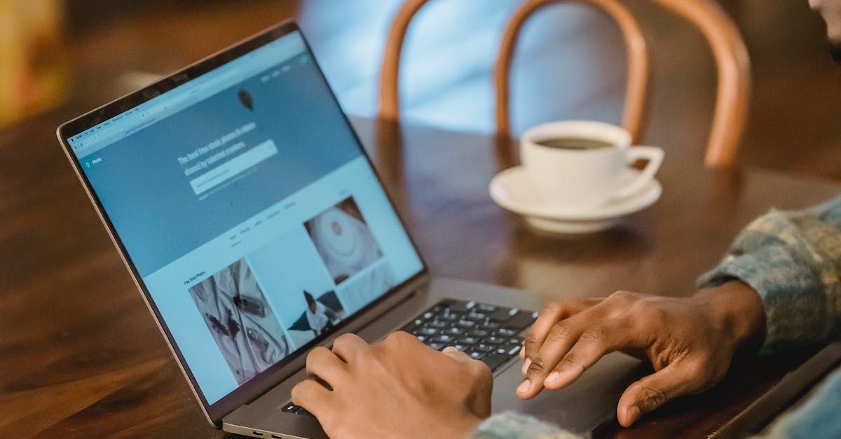 A person works on a laptop at a wooden table next to a cup of coffee.