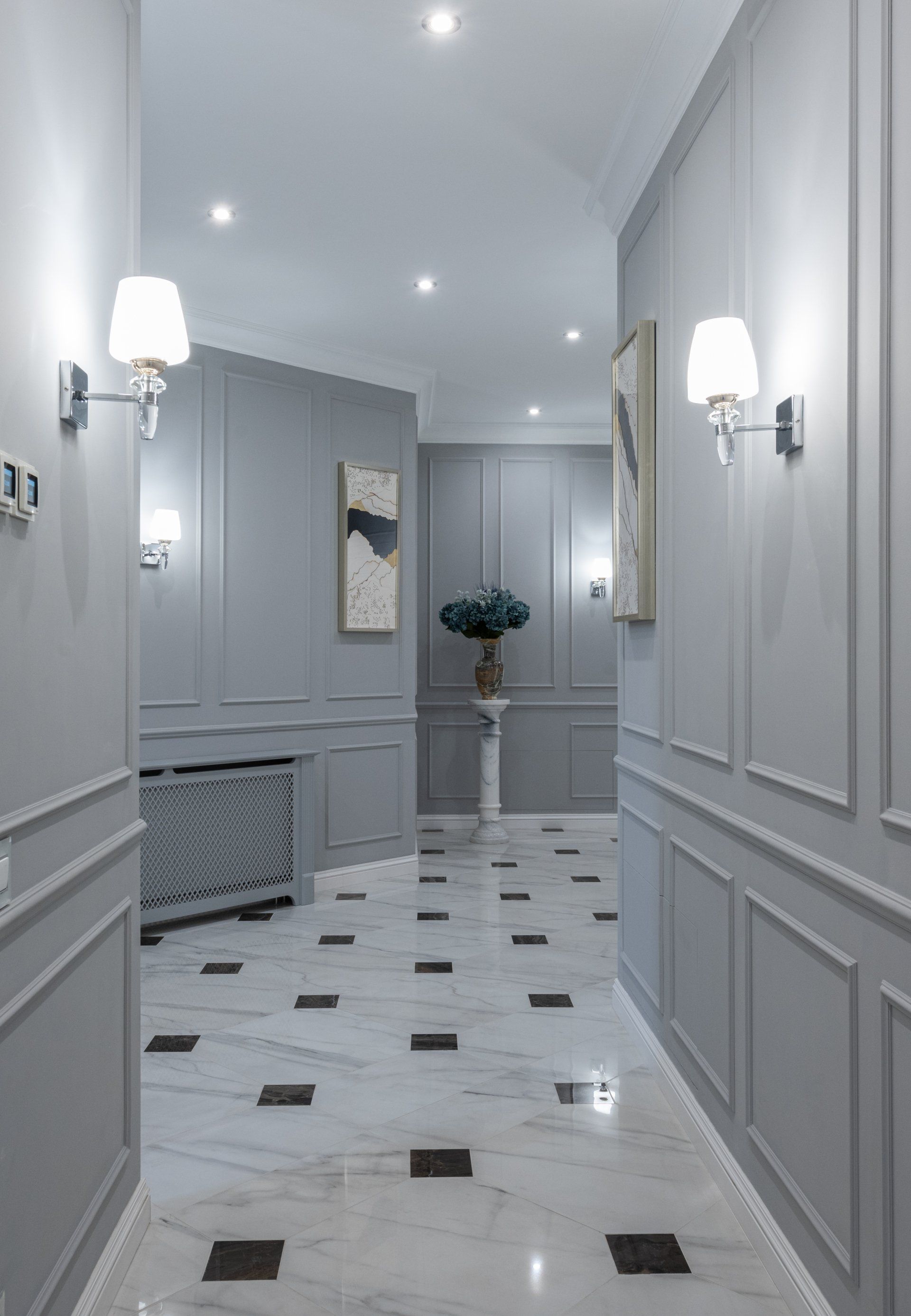 Gray hallway with white marble flooring, wall sconces, artwork, and molding.